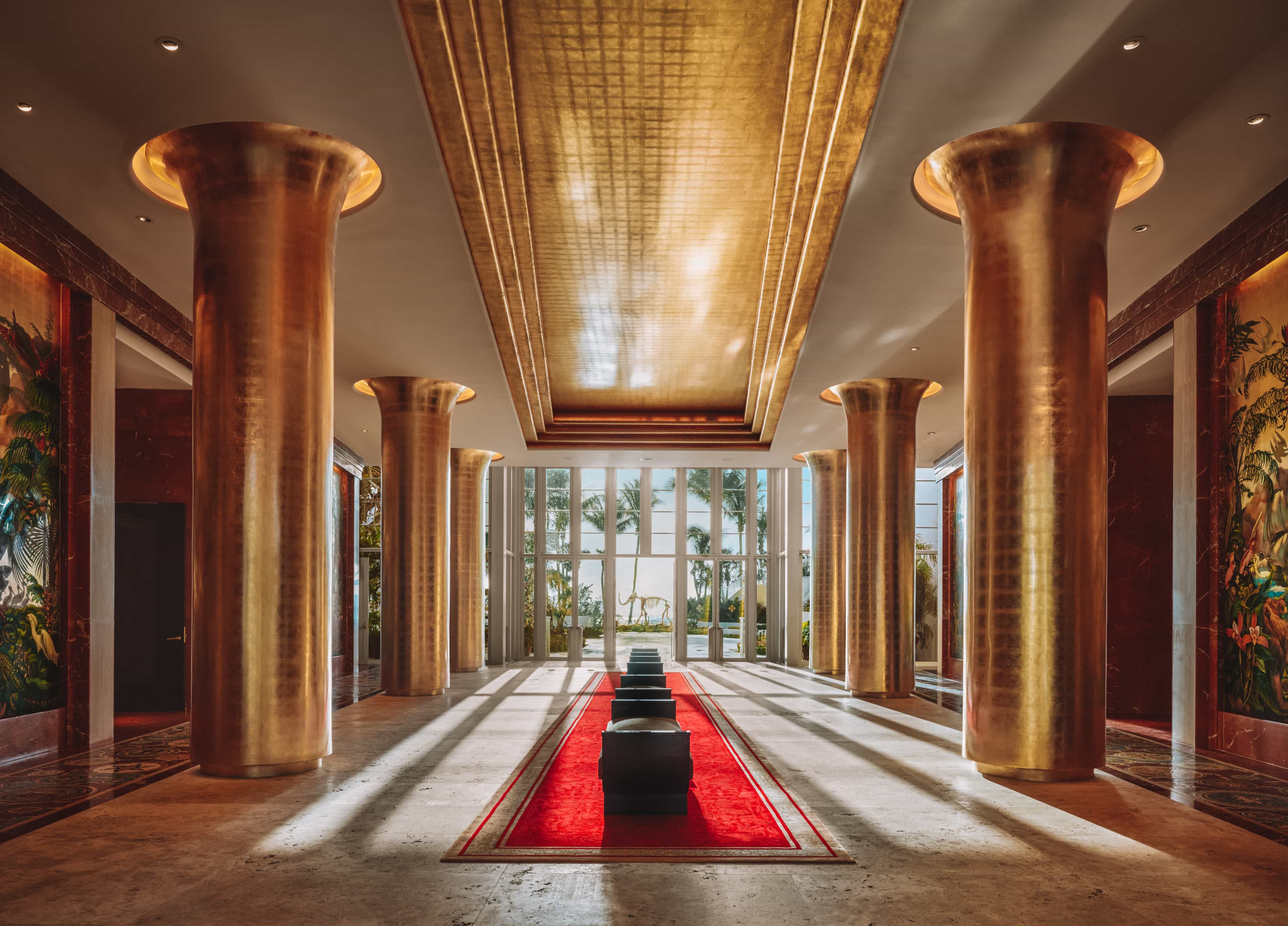a large foyer with tall windows, a red rug, and gold columns