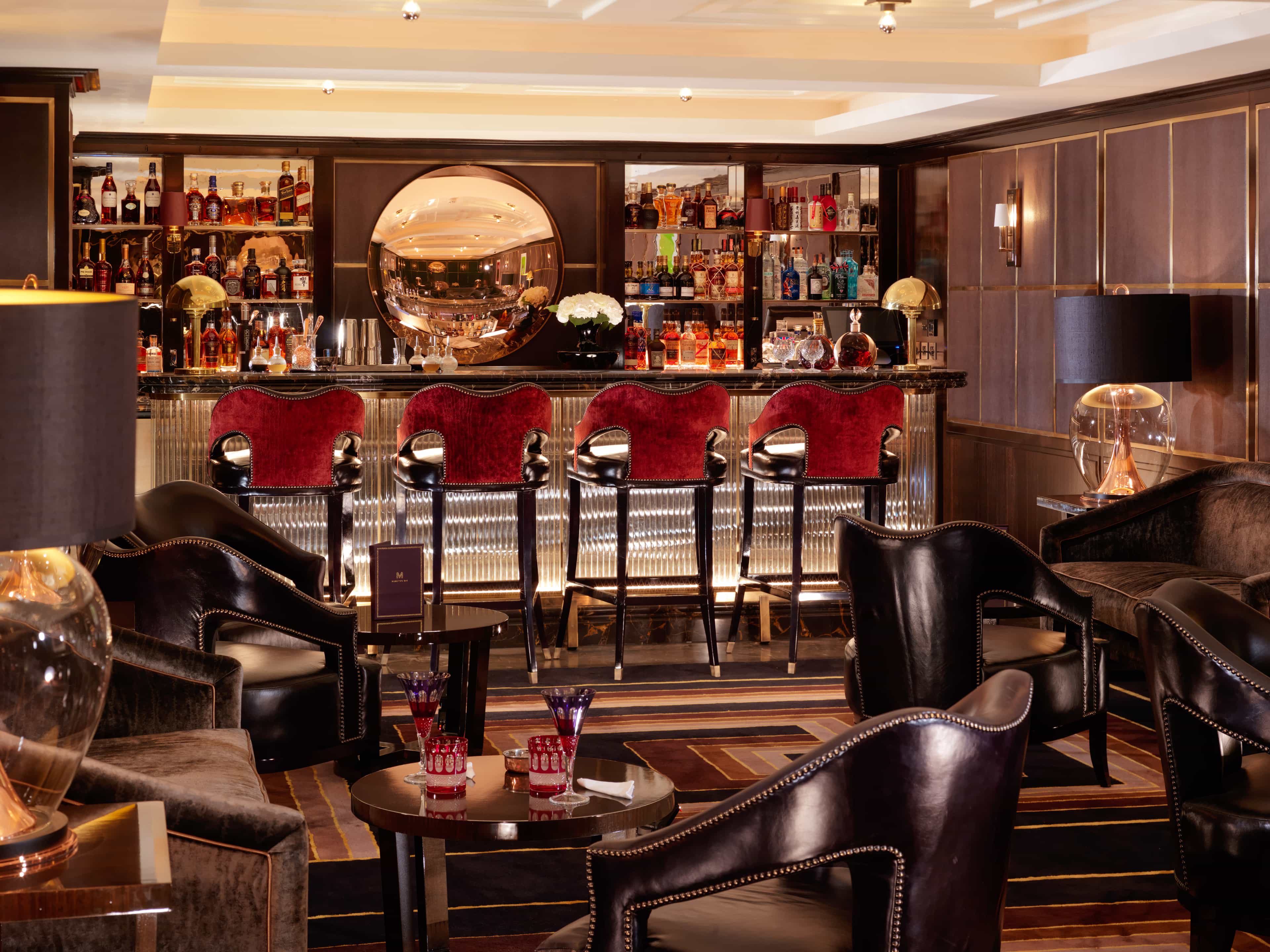 Plush lounge and bar with leather armchairs, red velvet barstools and brown paneled walls.