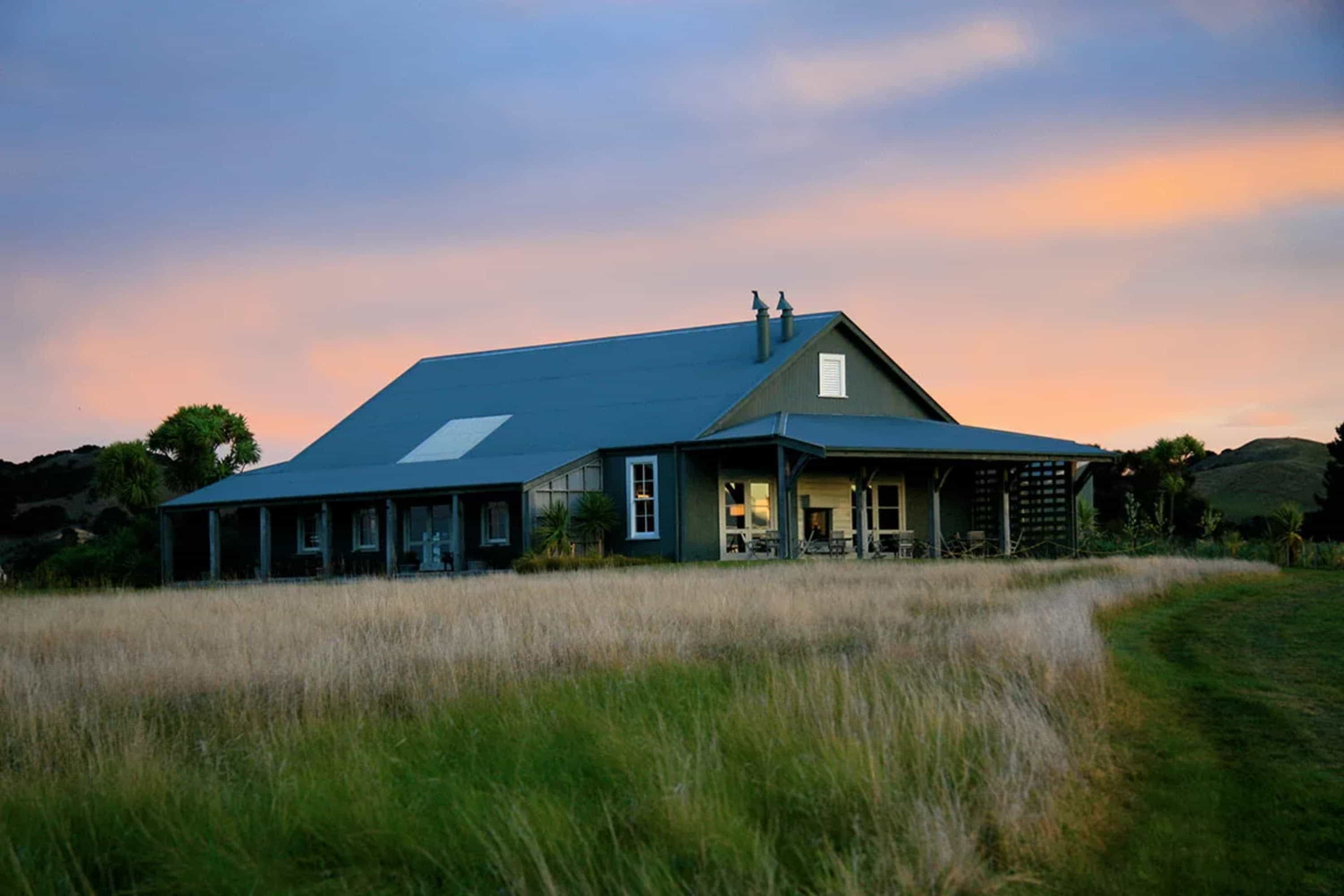 A large cabin surrounded by windswept grass at twilight