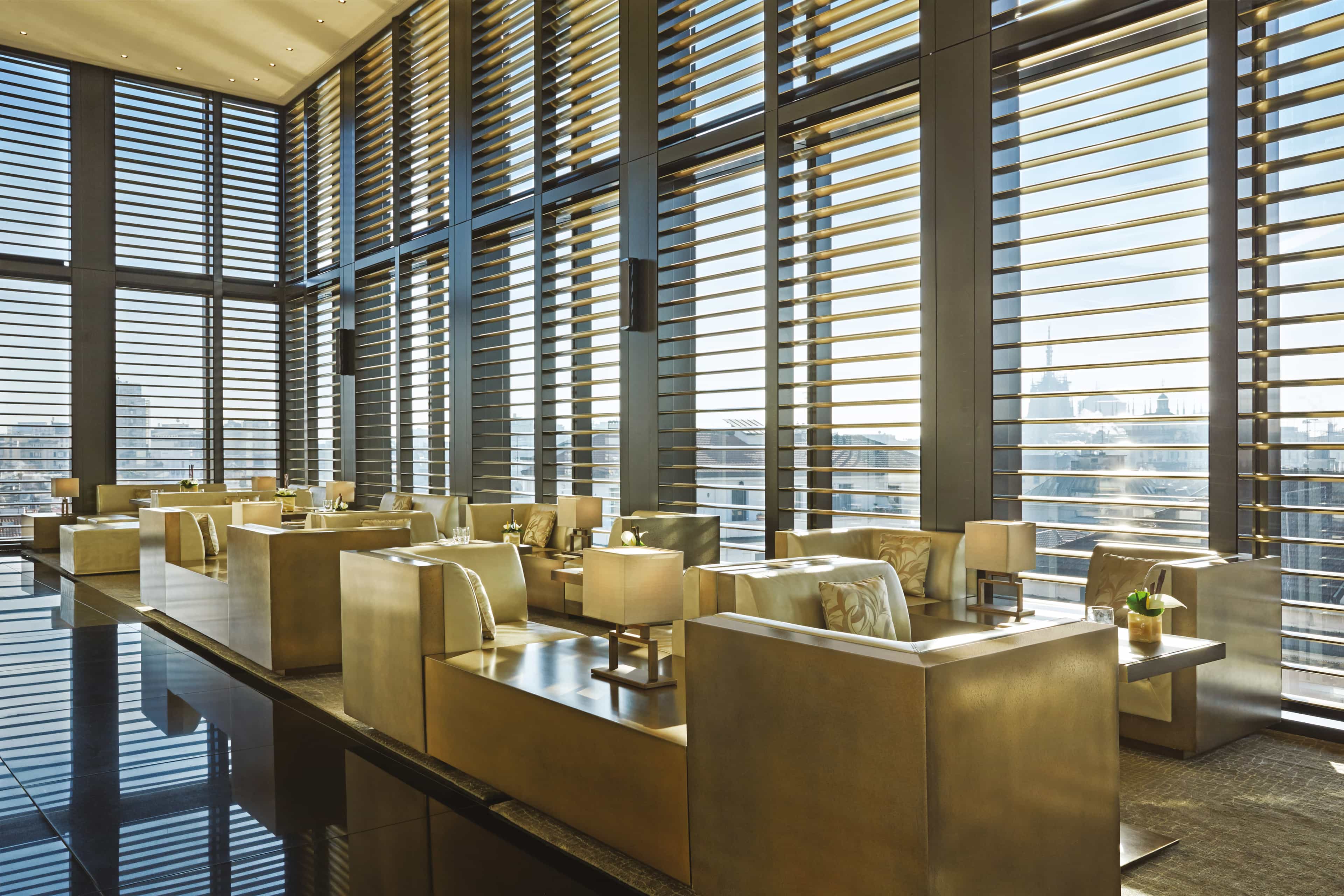 A sleek lounge with floor-to-ceiling windows, city views and gold furnishings