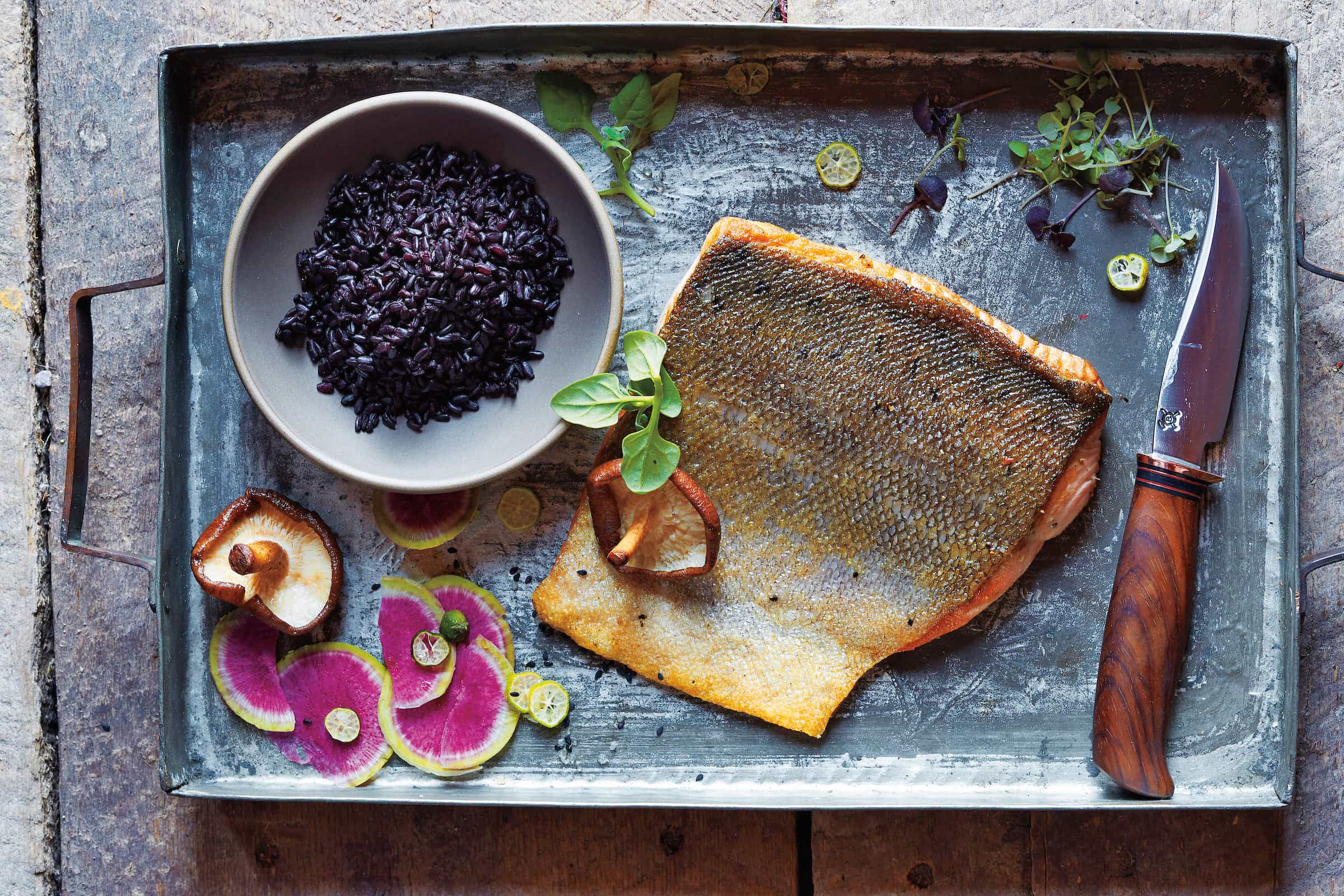 aerial view of a slab of salmon with a bowl of black rice and thinly sliced pink radishes
