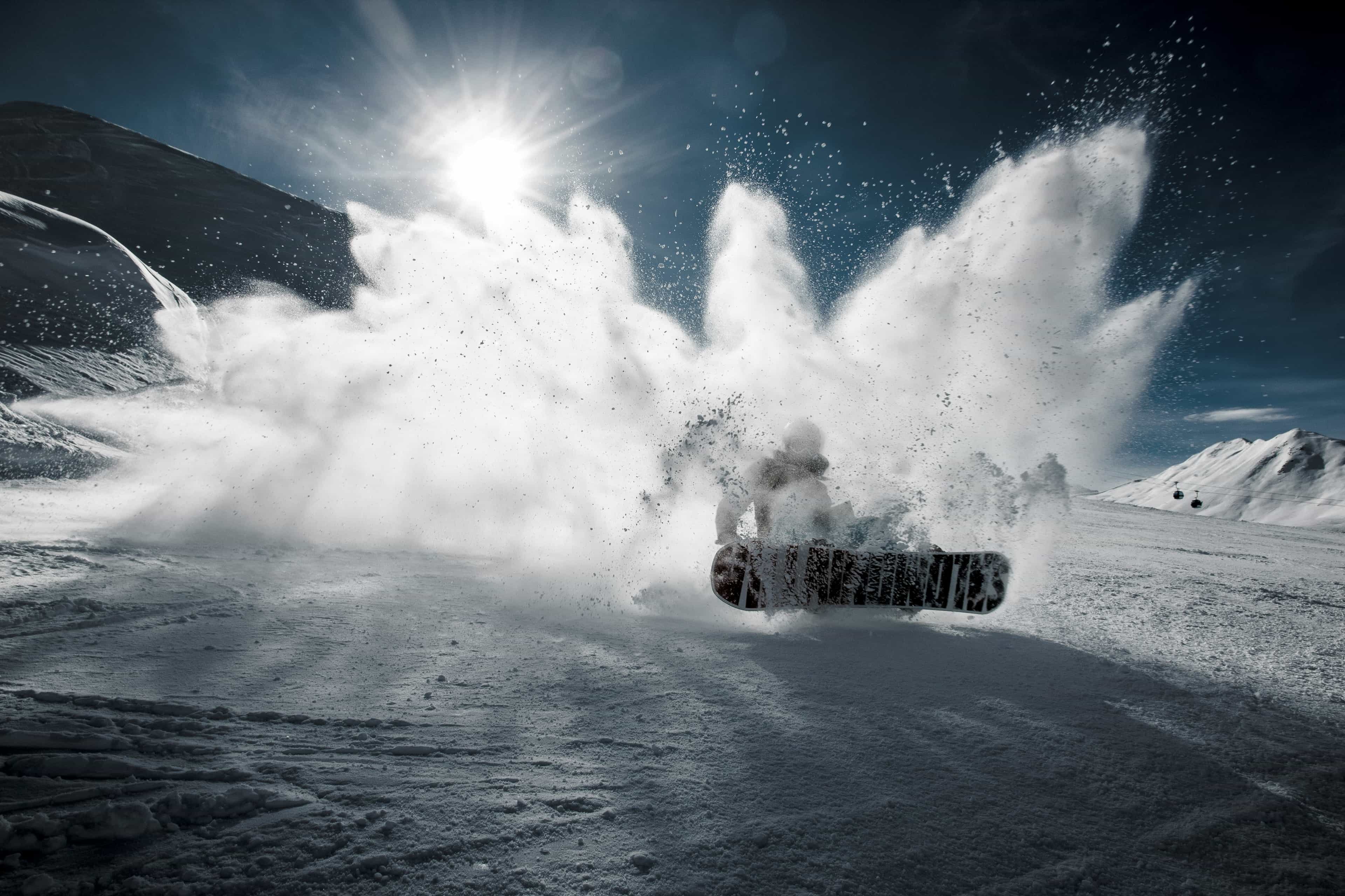 Snow being kicked up at the camera from a snowboarder with the sun shining above