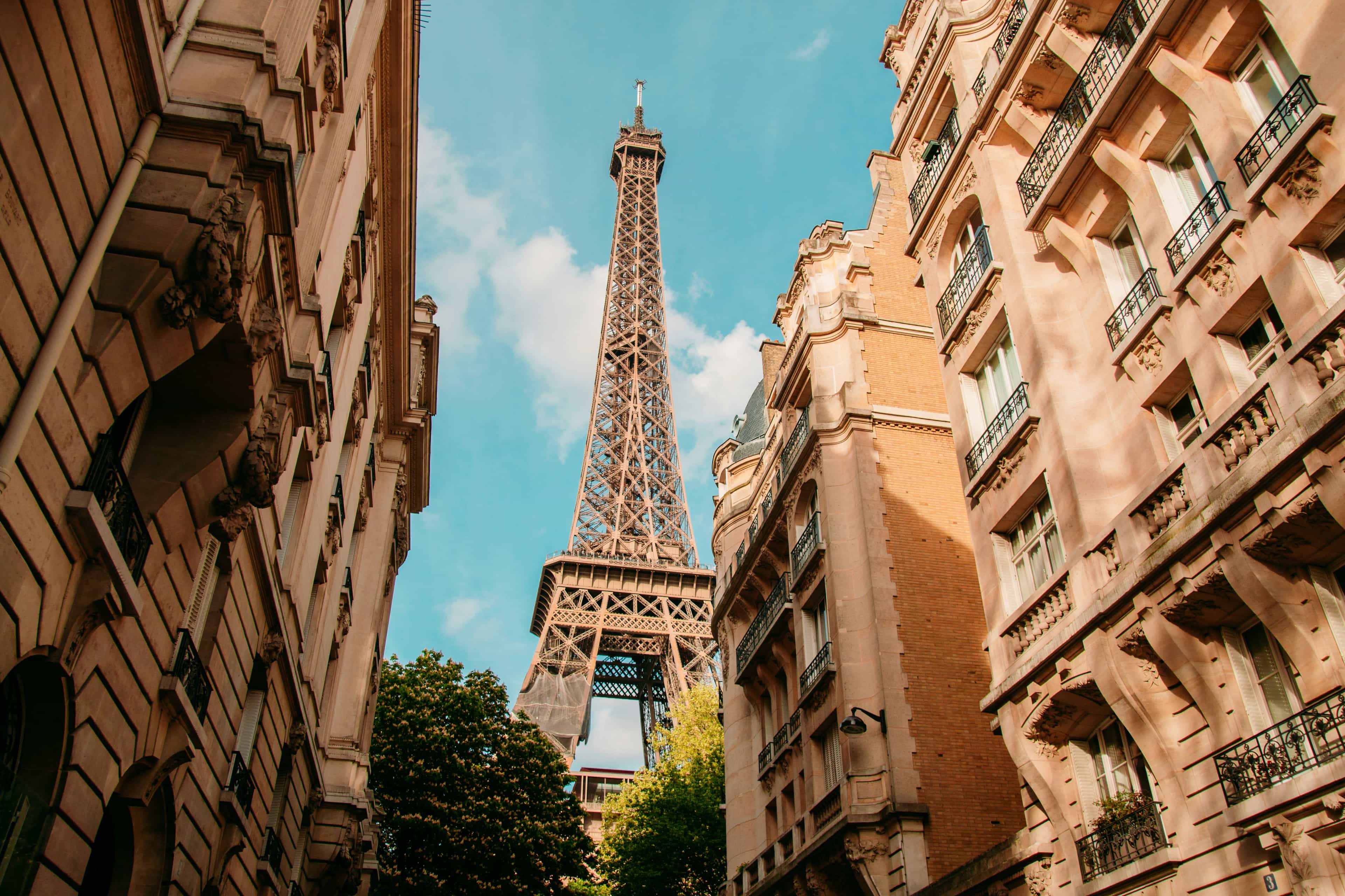 looking up at the eiffel tower in paris during daytime with brown apartment buildings on each side of the street