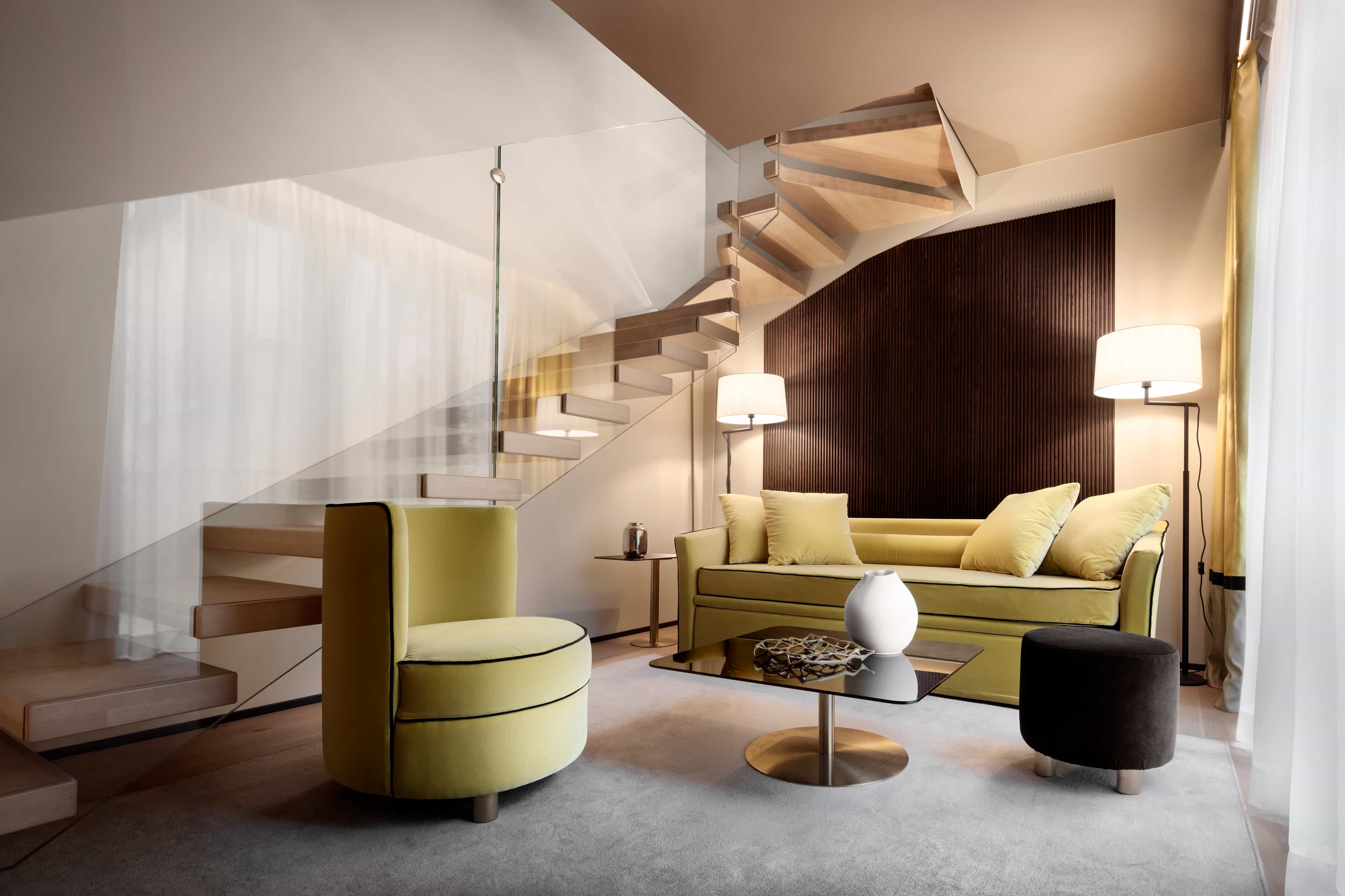 A contemporary suite with lime green seating and modern furniture with a winding staircase and glass divider