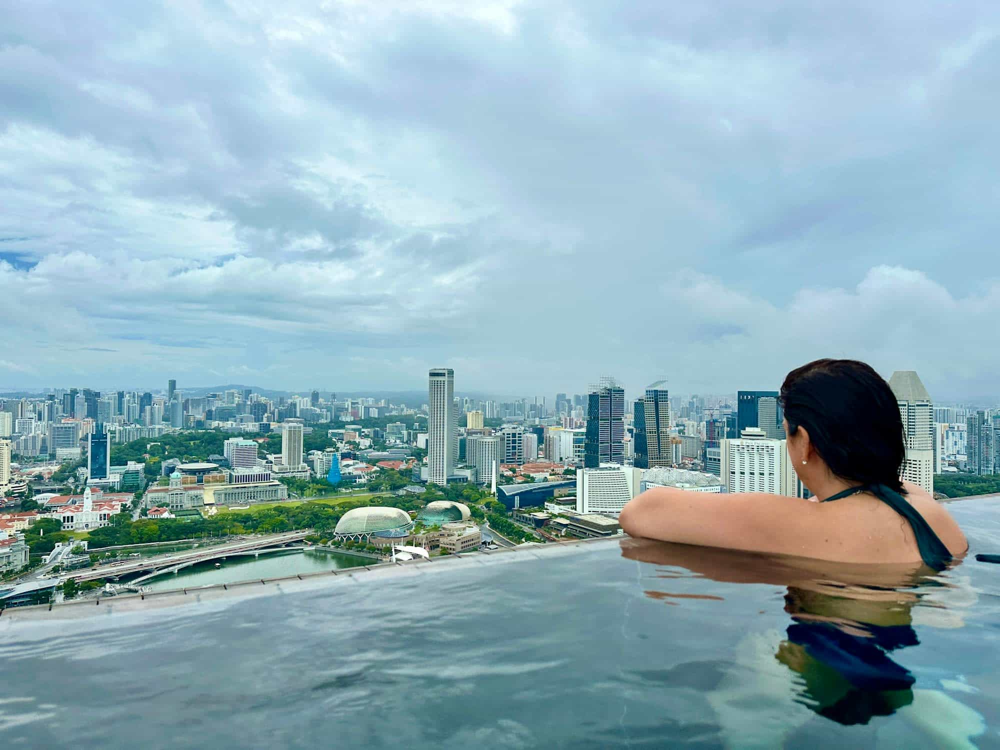 a woman sits in an infinity-edged pool overlooking a city