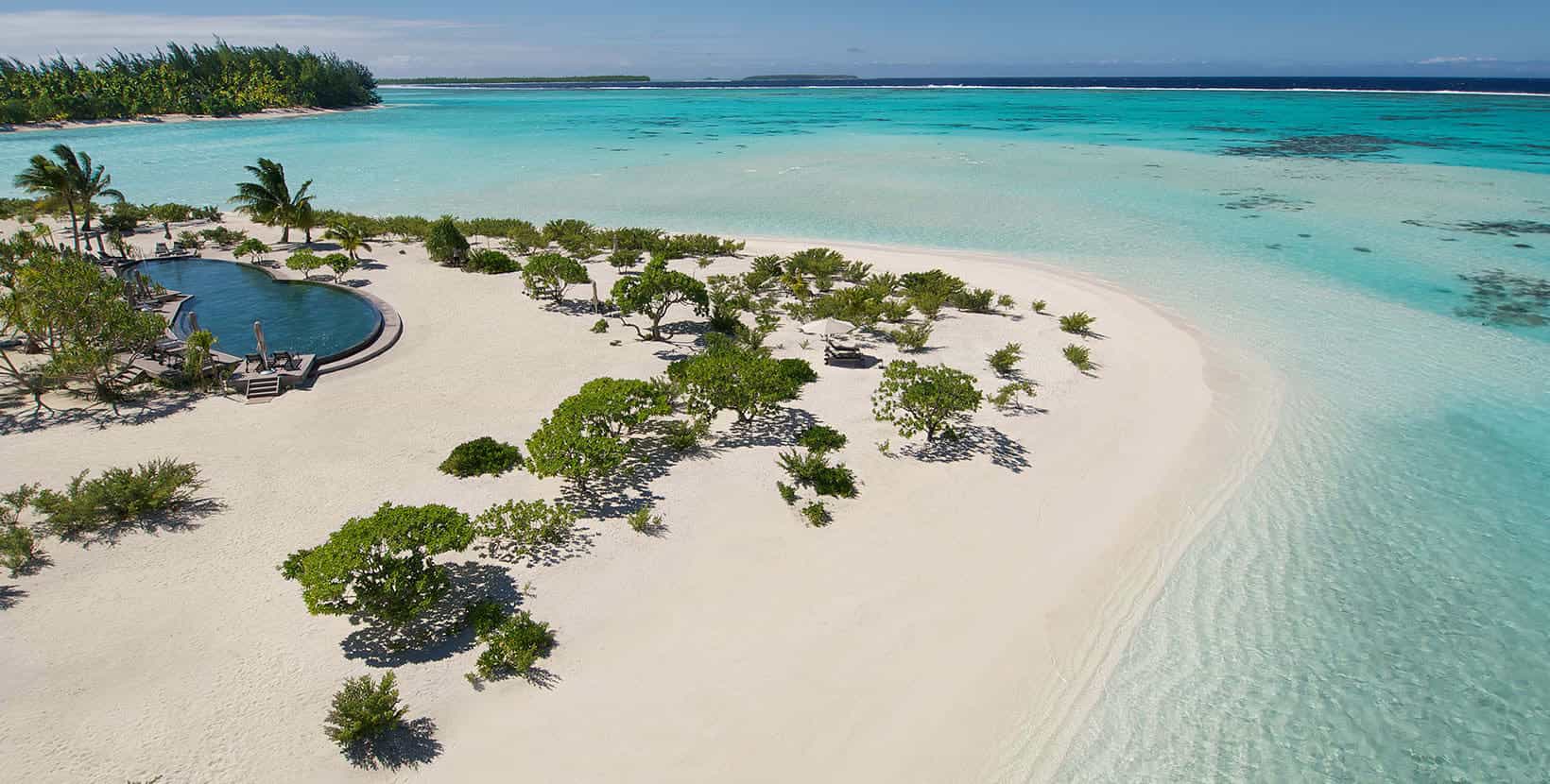 Aerial view of calm turquoise ocean, a white sand beach with some bushes, and a pool