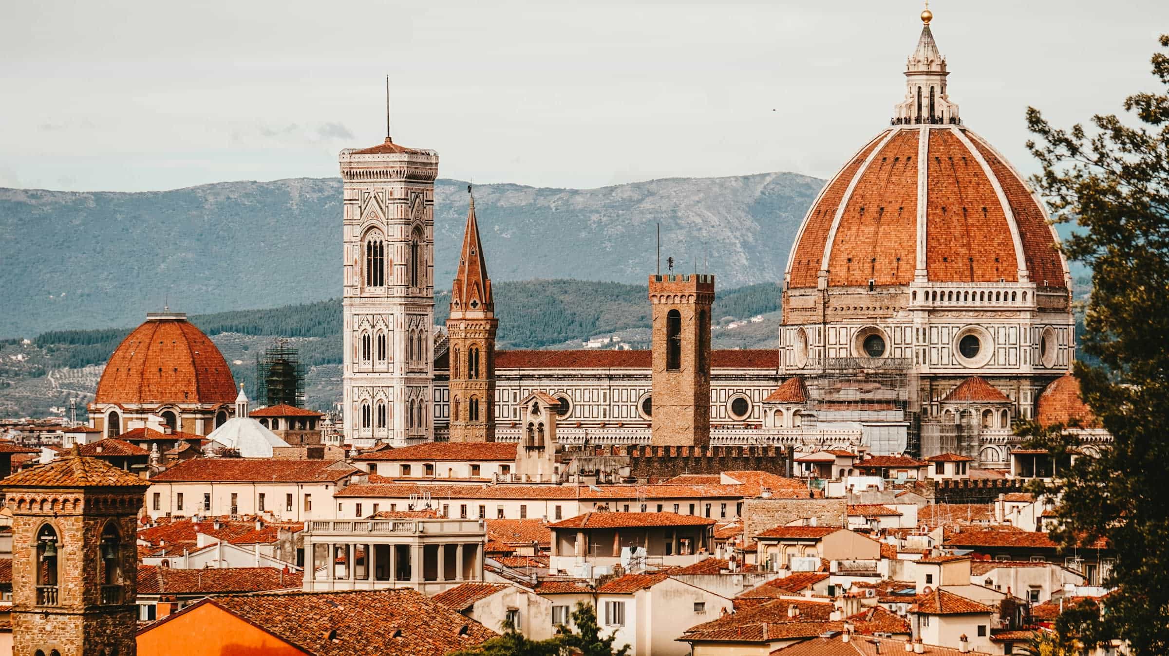 Brown domed building with tower and tan rooftops with hills in the background