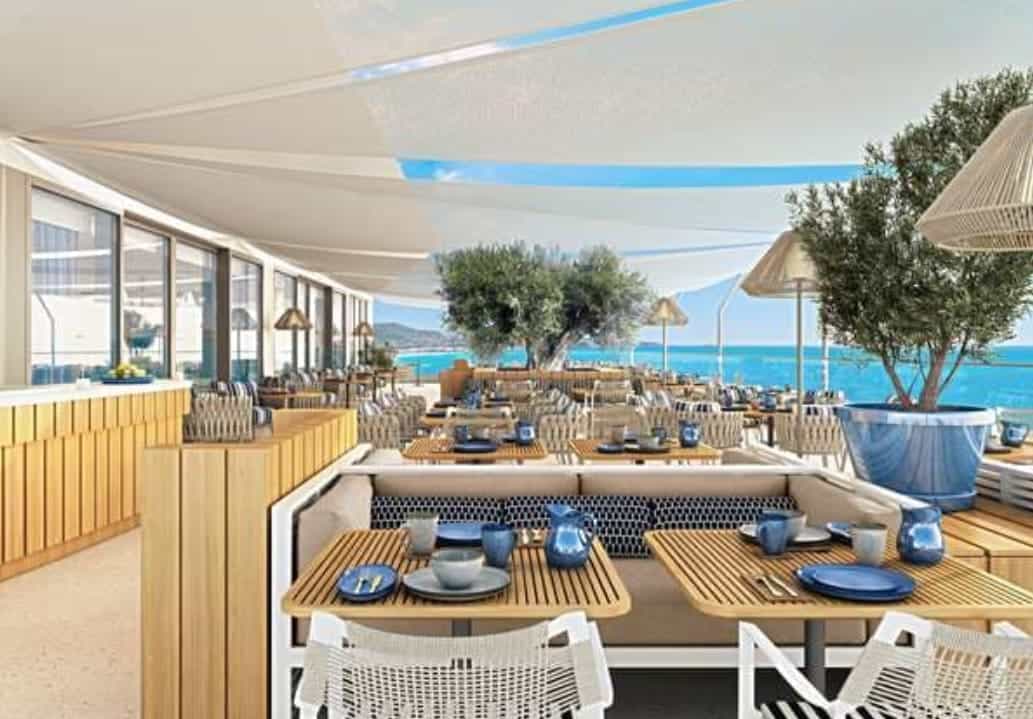 A hotel dining terrace with ocean views and wood and white furniture