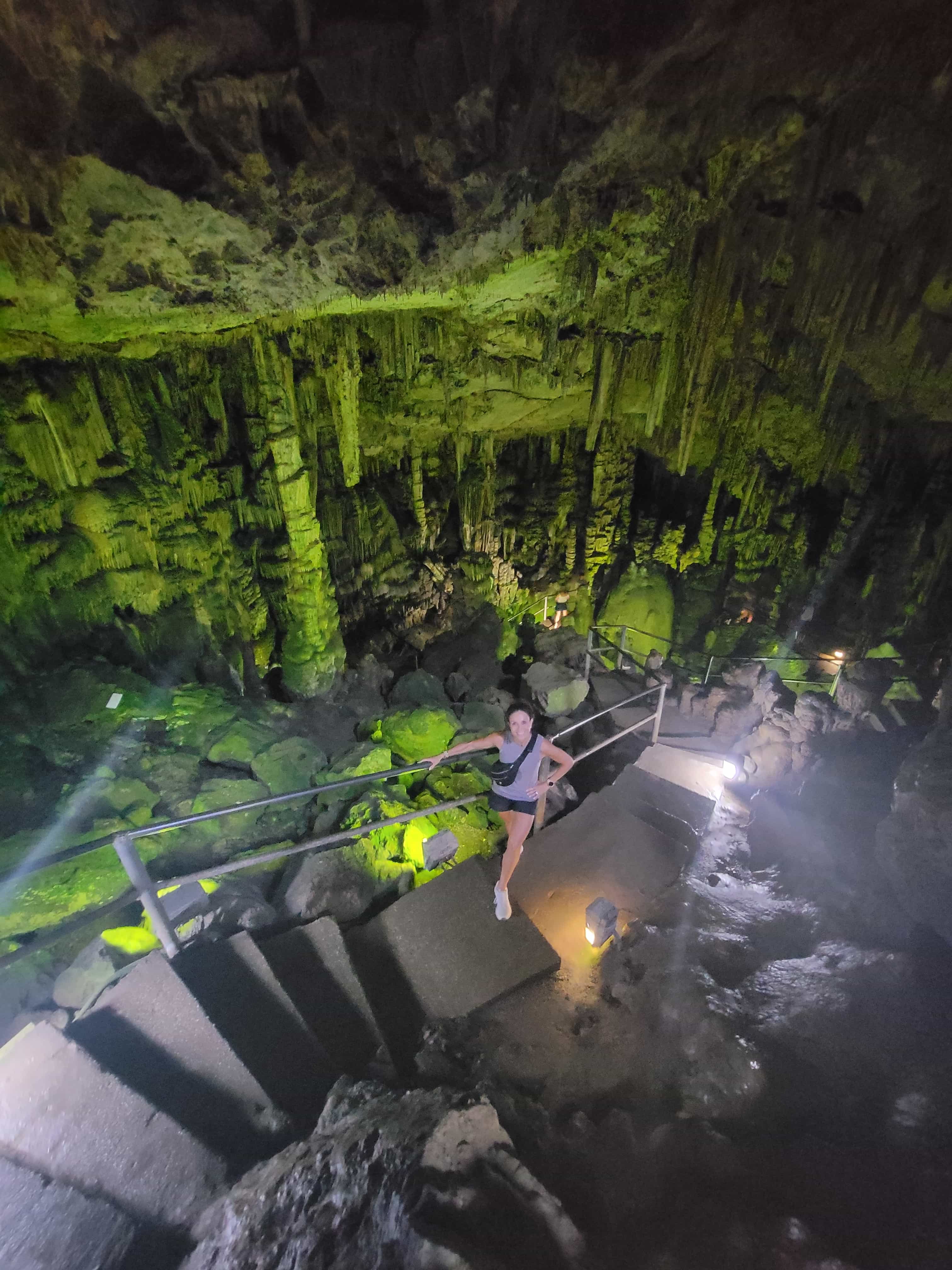Travel advisor Laurie standing on stairs in a cave illuminated with green lighting.