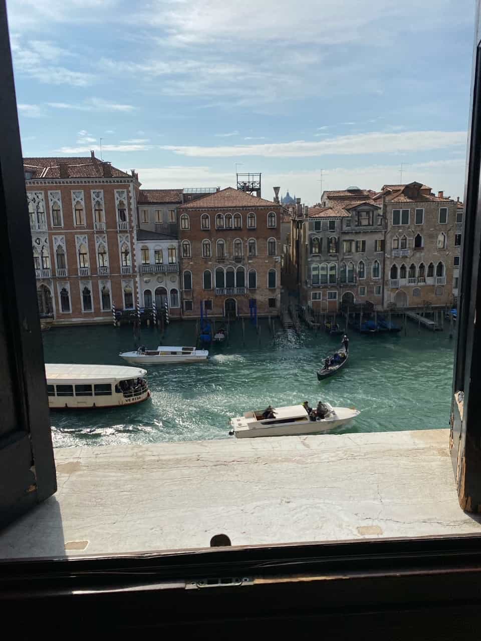 A view through a window of a water way with boats and beautiful buildings across the water way. 