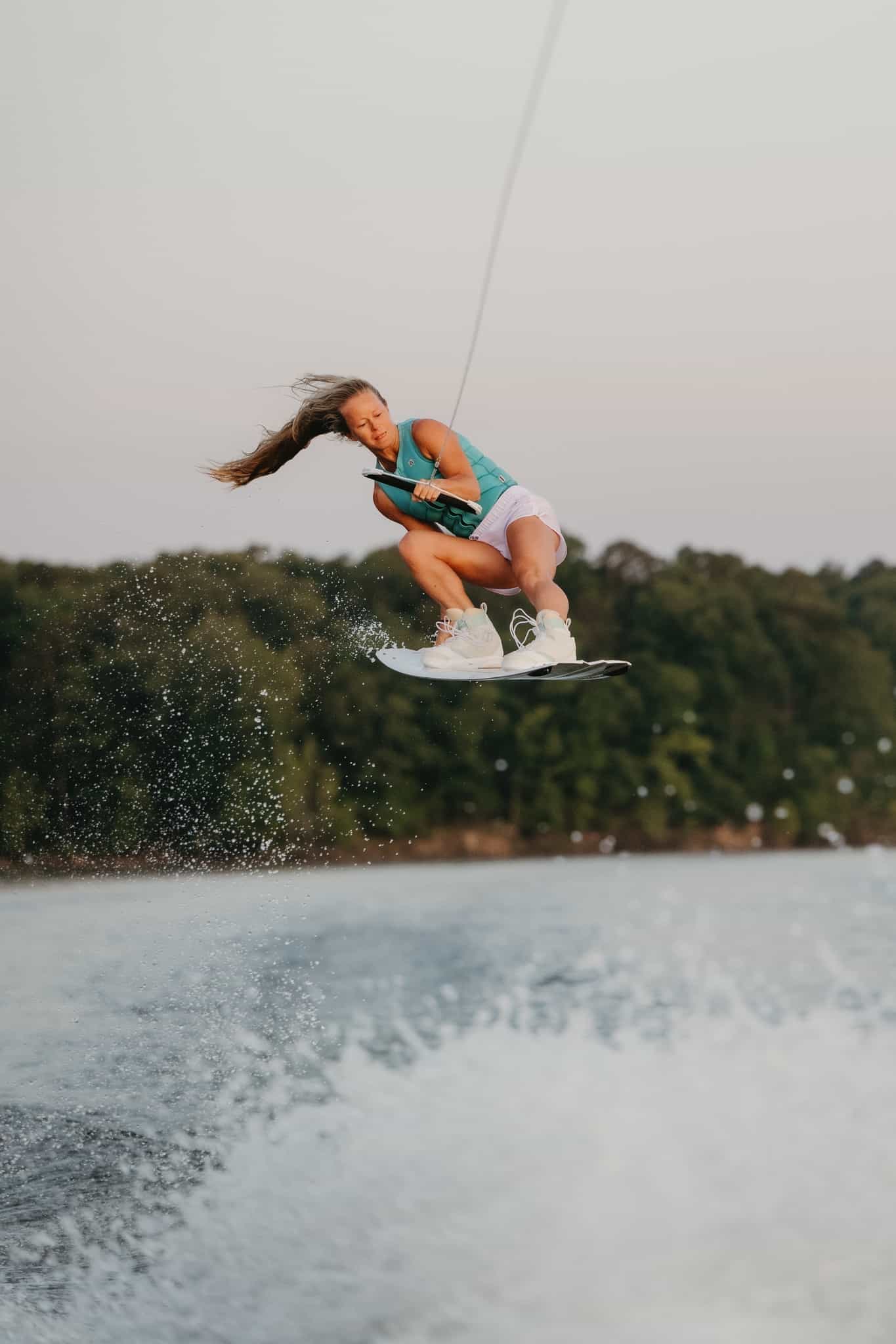 Maggie airborne while wakeboarding on a lake on a cloudy day