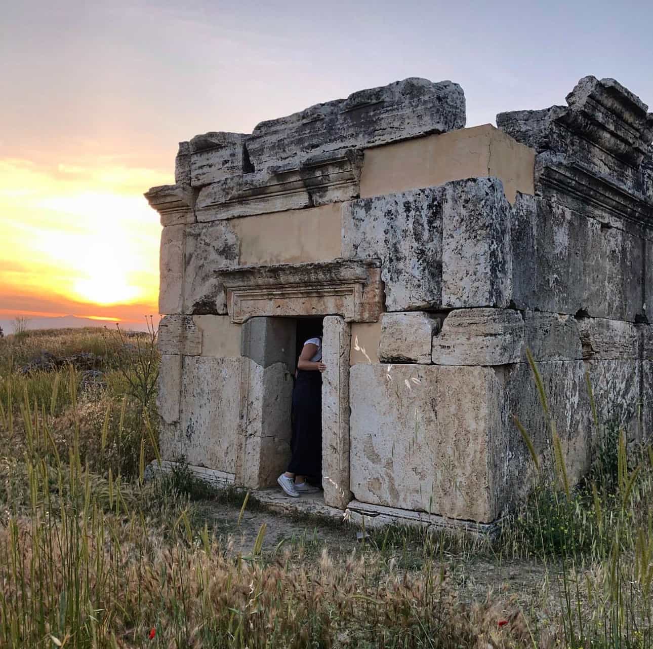 View of an old stone structure in the middle of a grassy field at sunset