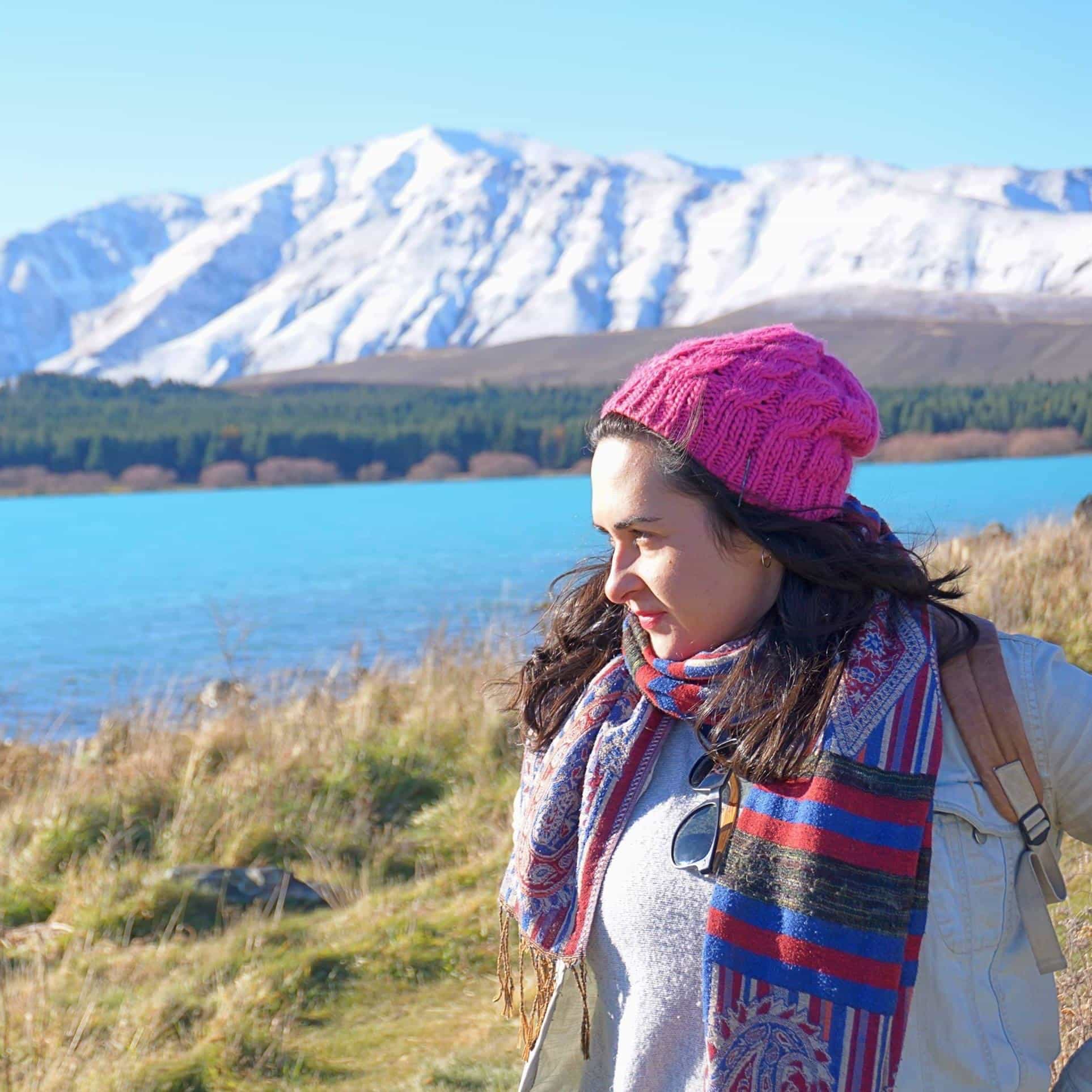 Advisor in a pink knit cap and scarf in front of a lake with a large mountain range behind her