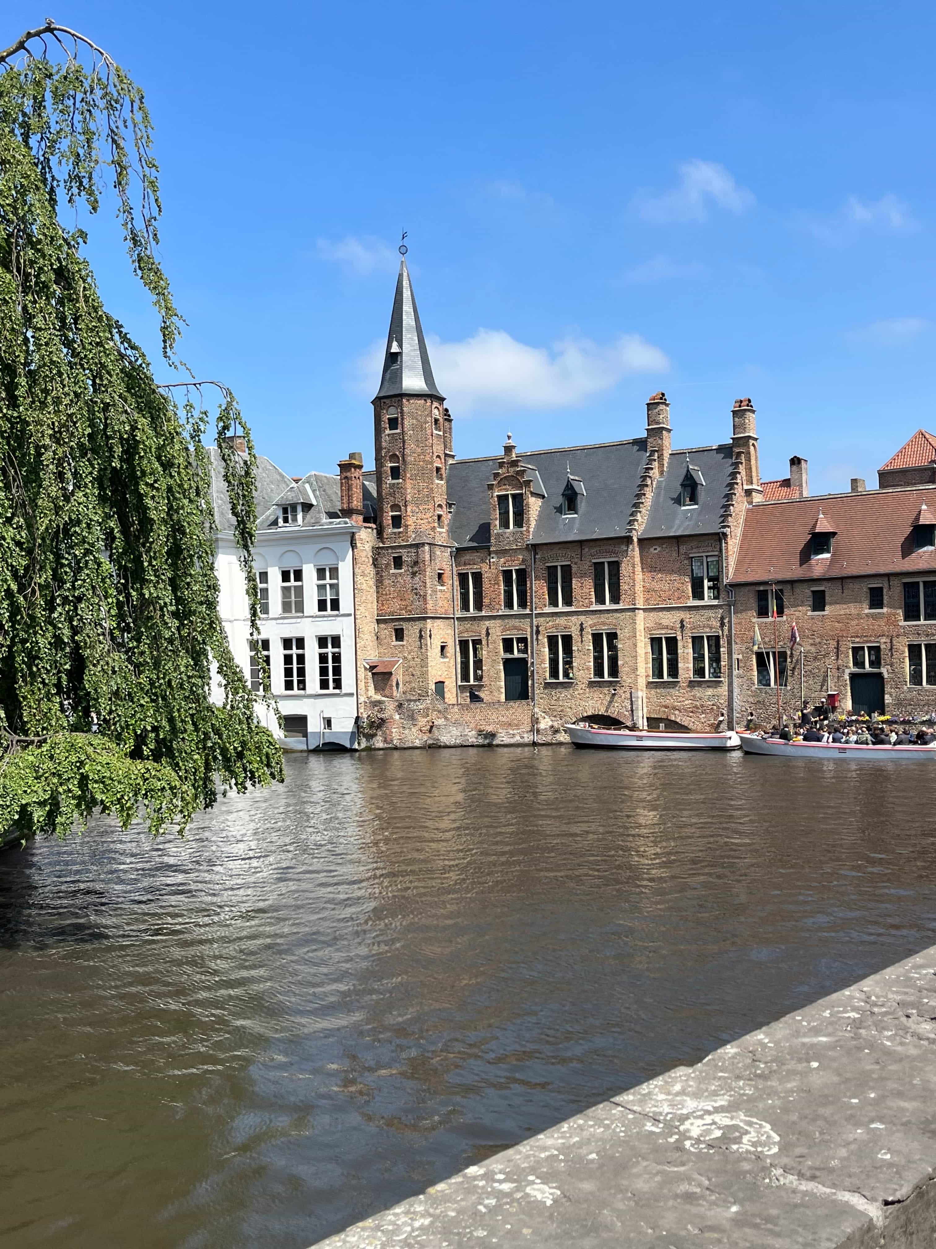 View of an old stone tower and nearby buildings along a canal under sunny skies