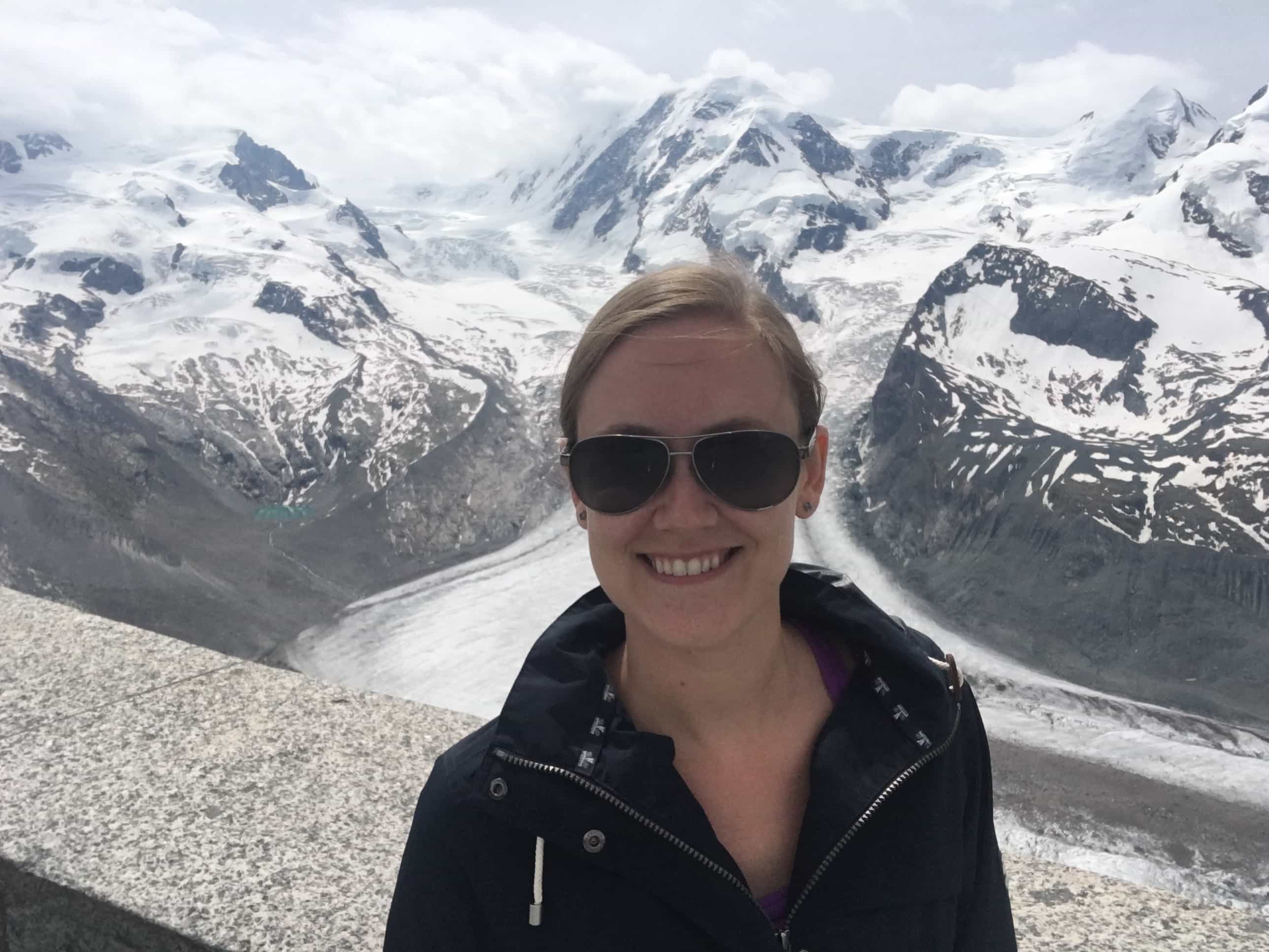 Advisor posing on a mountain with snowy peaks behind her.