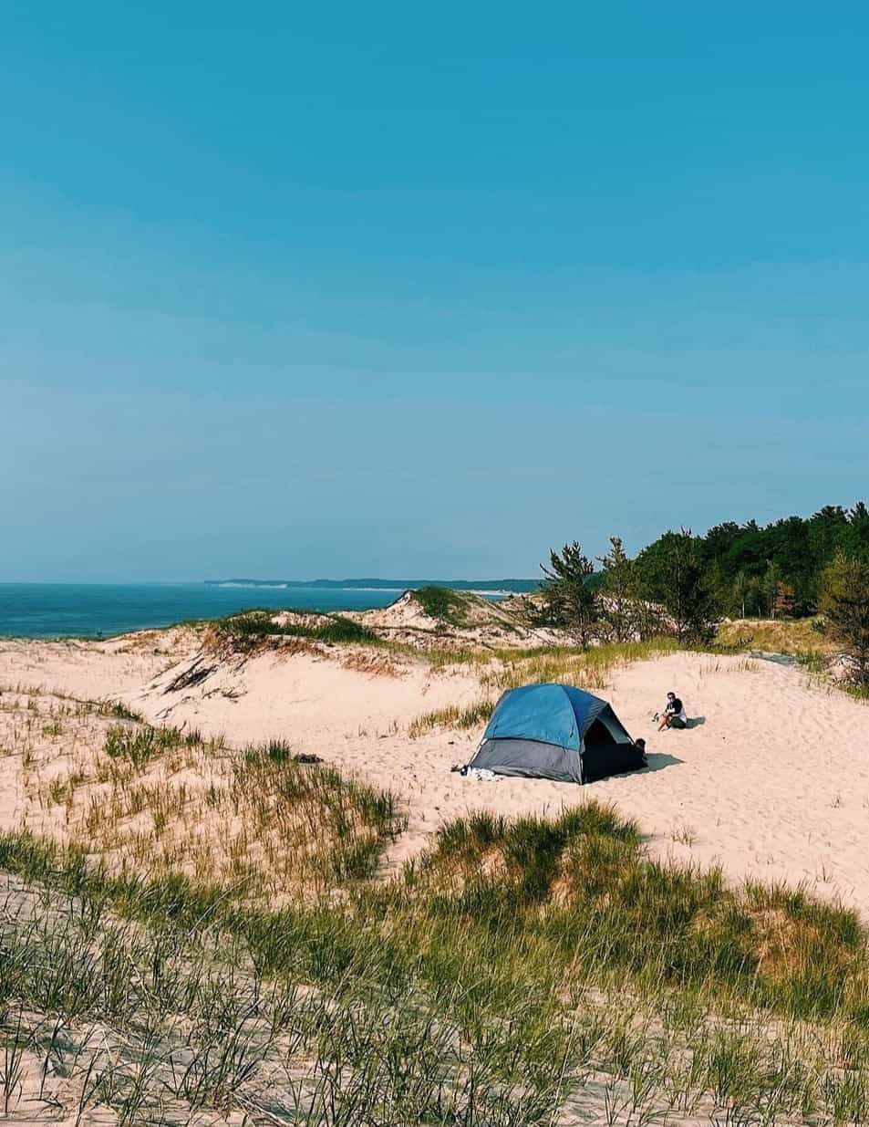 View of a blue tent pitched on the sand with the sea visible on the horizon
