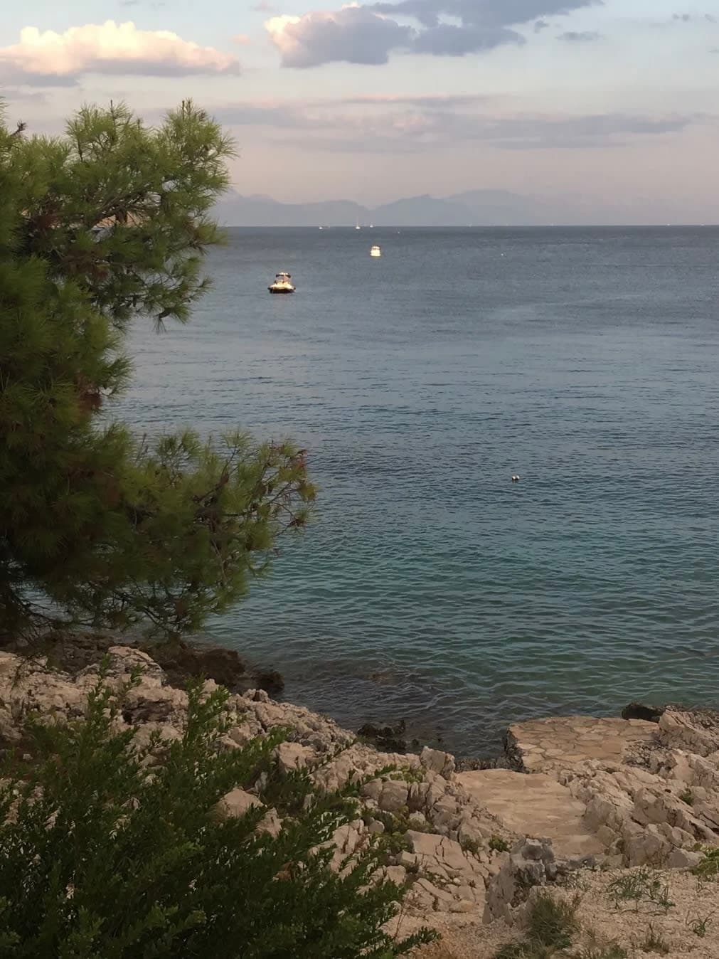 Beautiful view of rocks meeting a calm sea with a boat floating in the distance