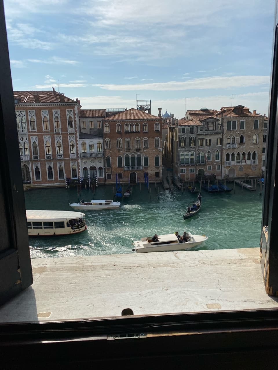 A view through a window of a water way with boats and beautiful buildings across the water way. 