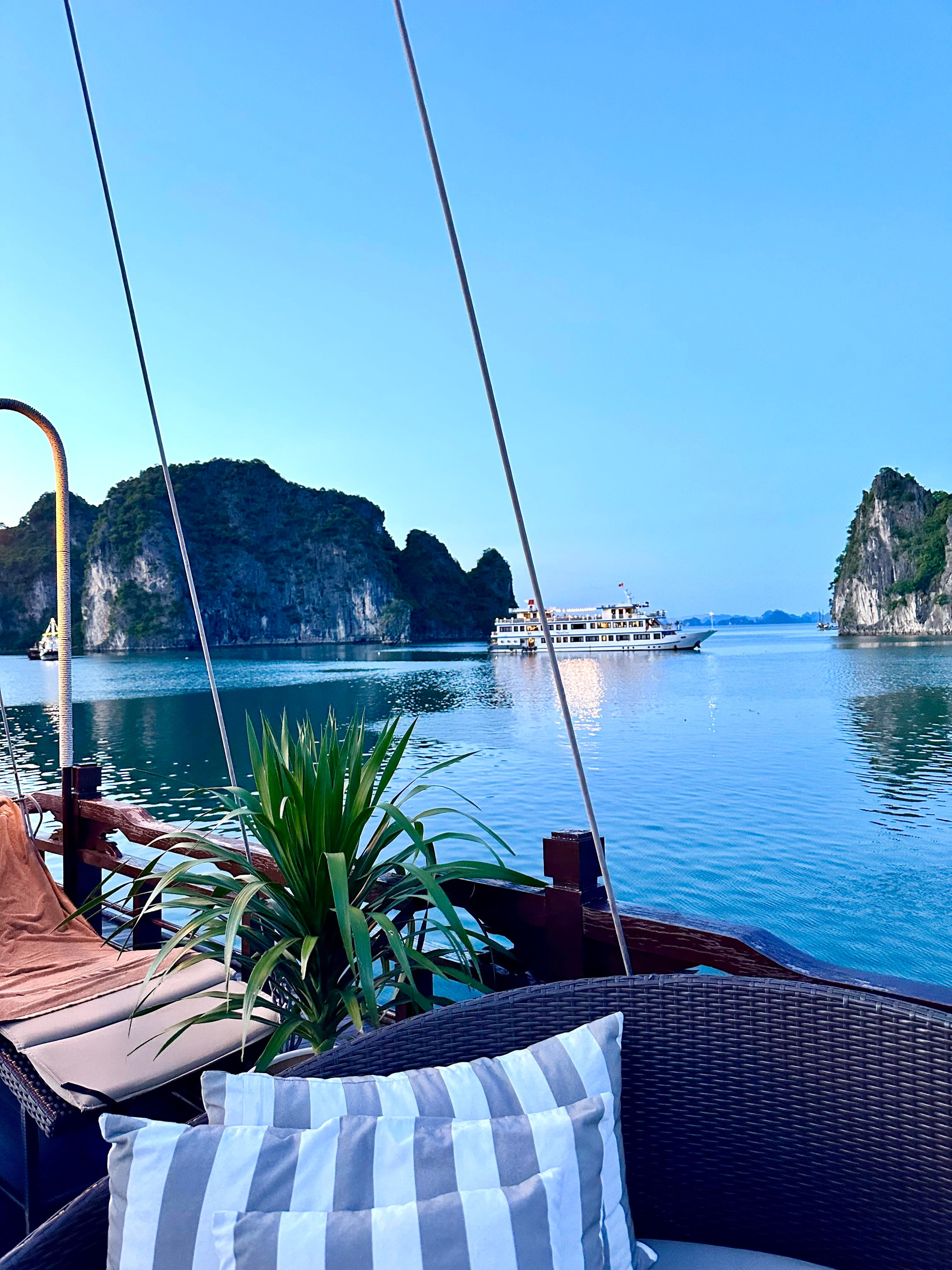 Pretty view of a striped chair on a boat deck with plants floating at sea with another boat and rocks visible in the distance