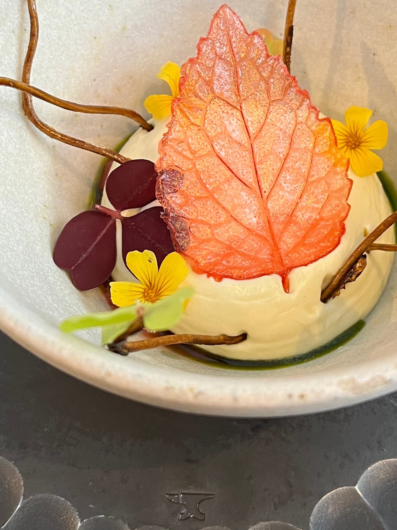 View of a beautifully decorated dessert with a faux leaf and branches in a bowl on a table