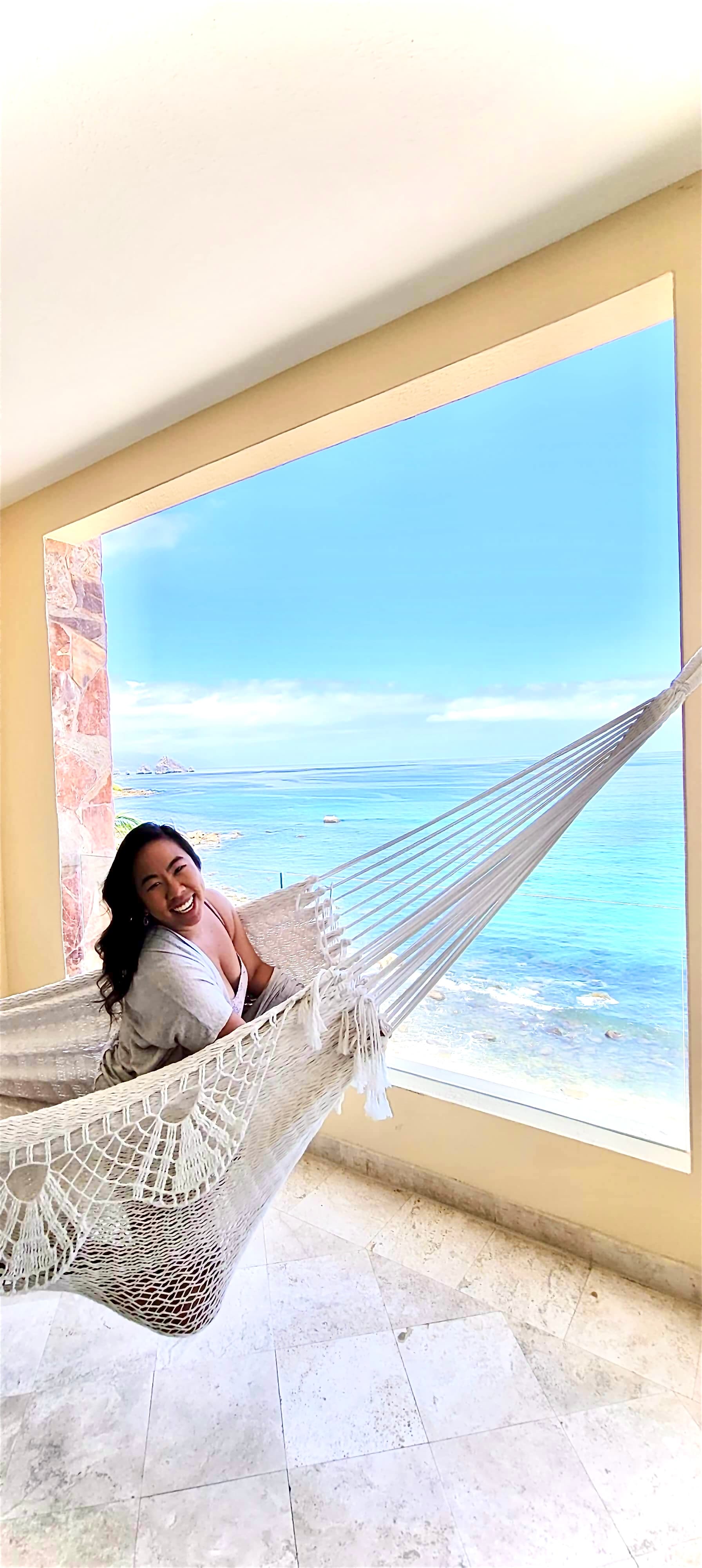 Chelsey sitting in a hammock looking out of a window with ocean views seen in the distance