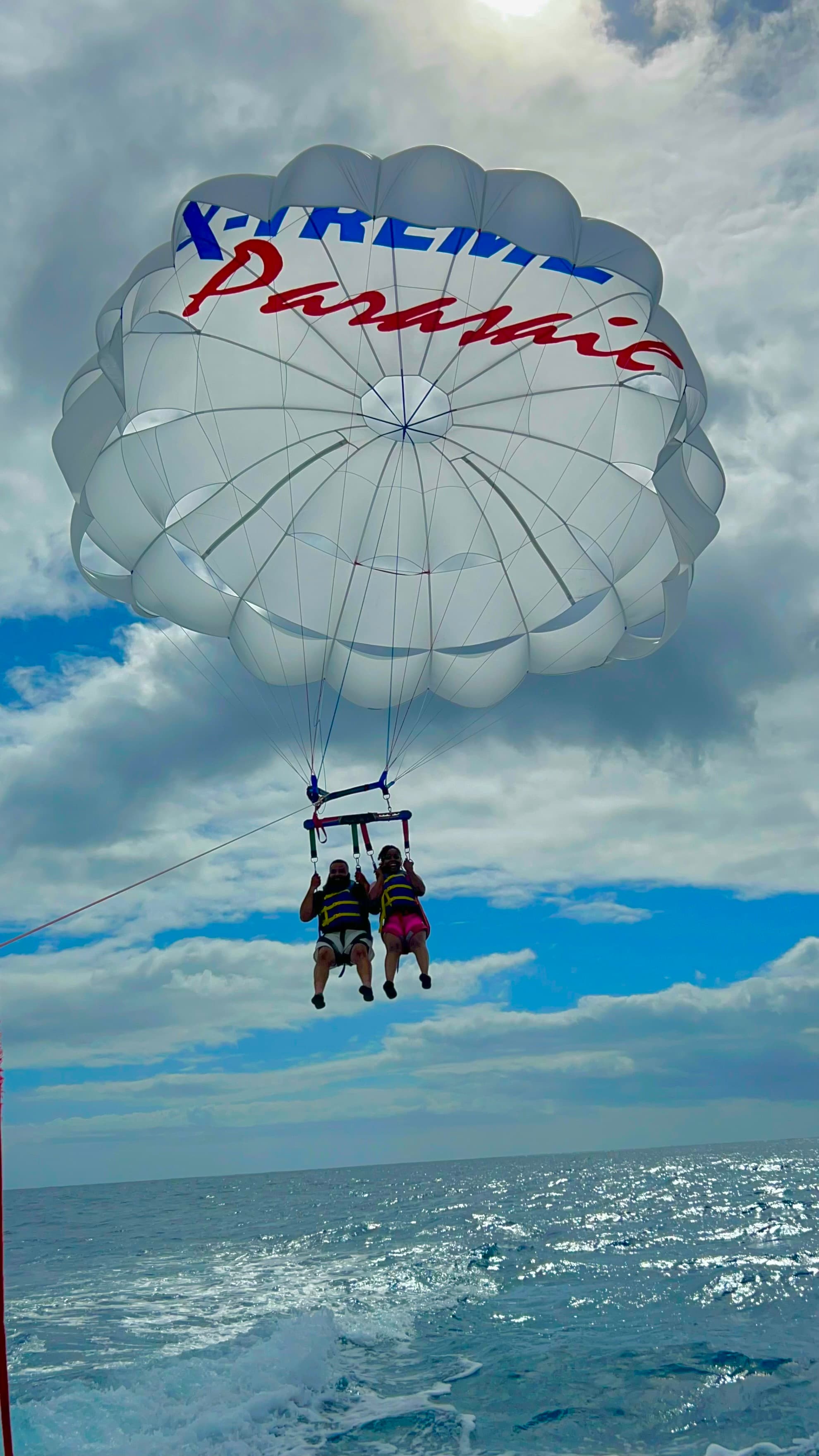 Two people hovering above the ocean with a large white parasail above on a sunny day