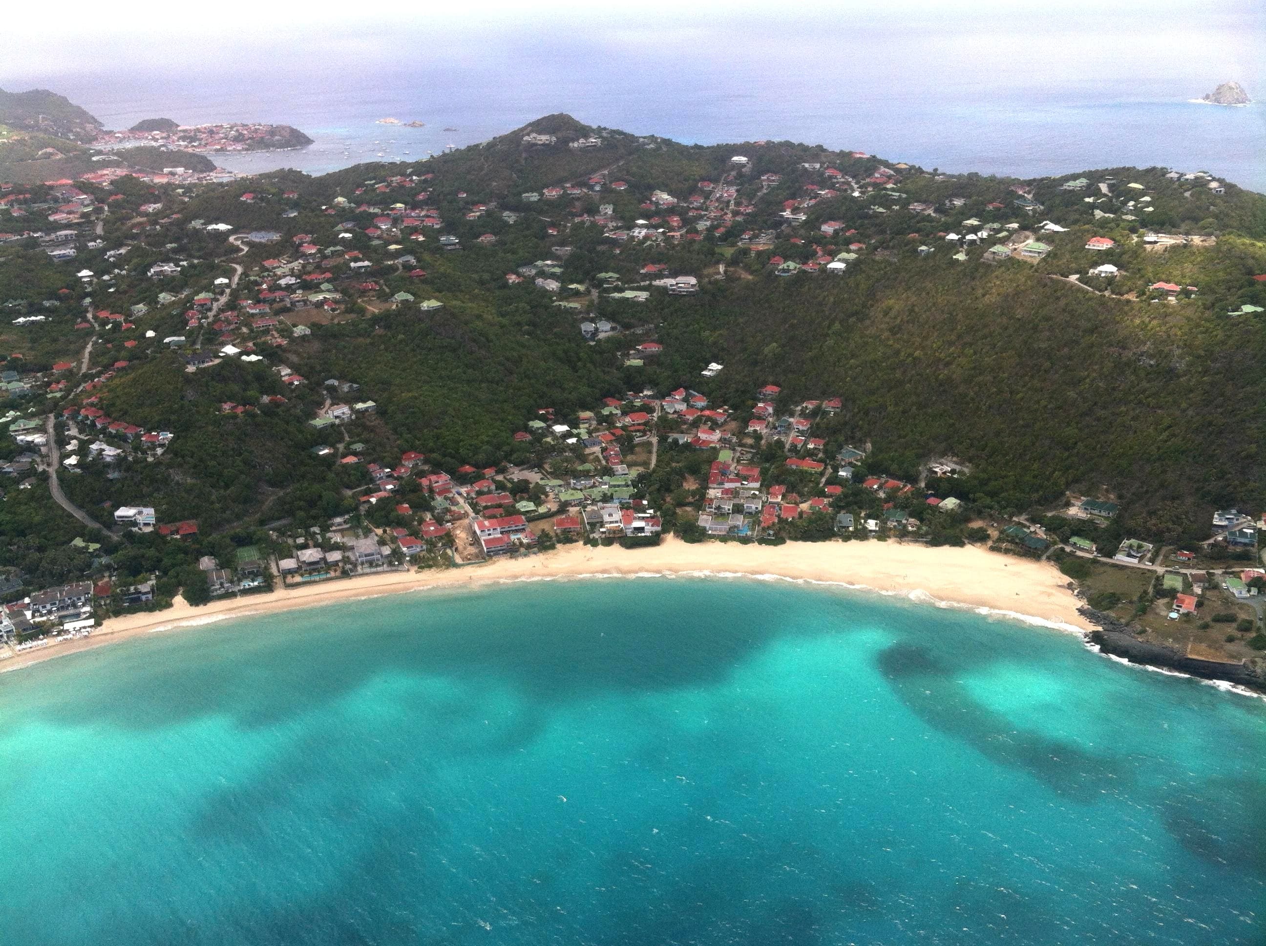 Aerial view of a beautiful white sand beach and clear ocean with small buildings dotting the green coastline