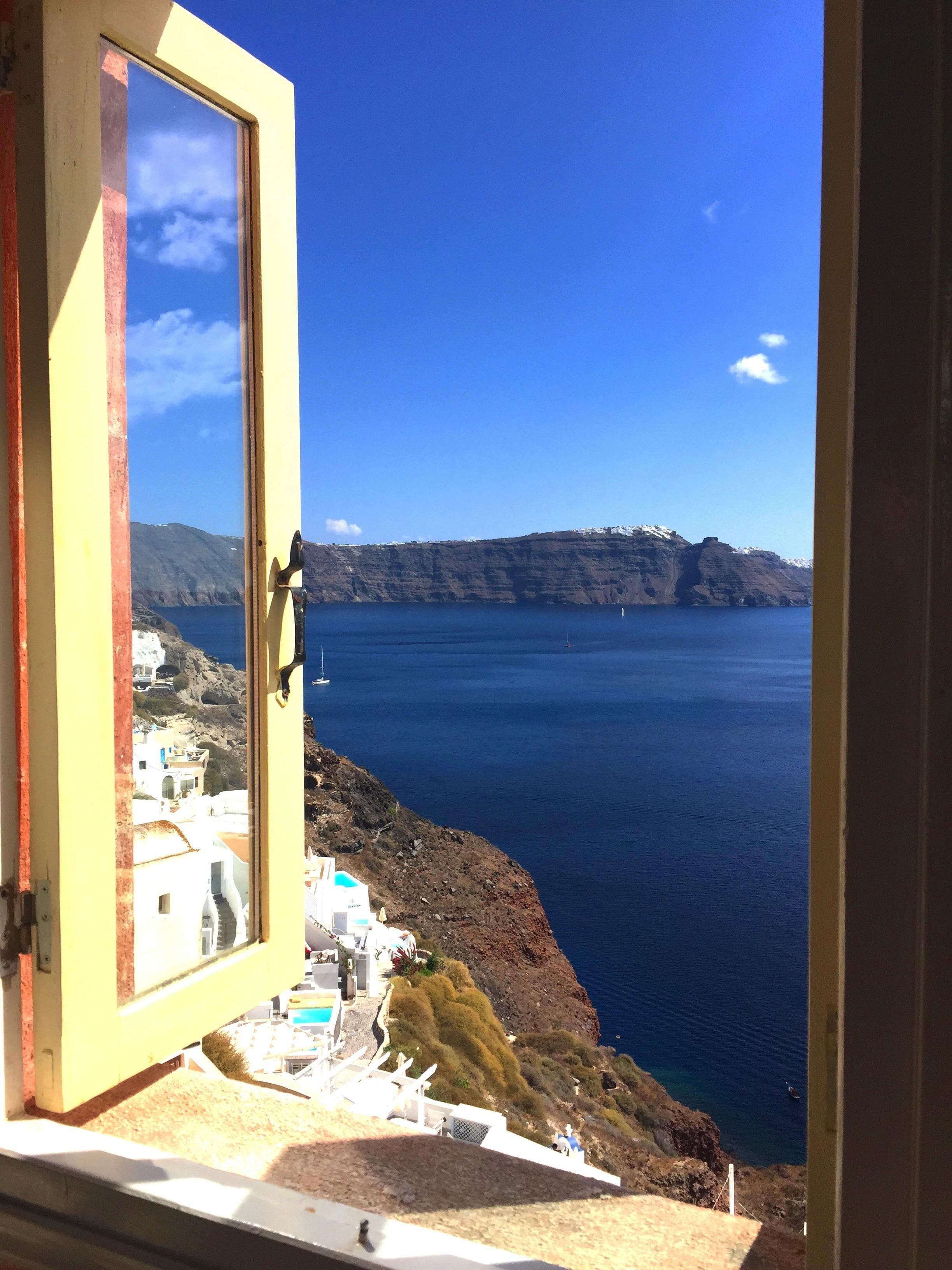 View of a beautiful deep blue ocean and hilly coastline seen through an open window on a sunny day