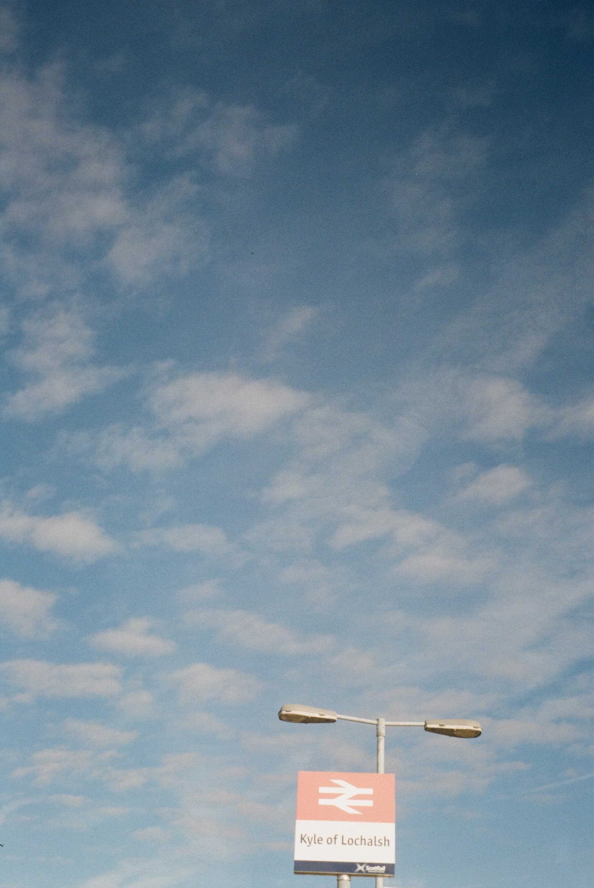 View of a red and white sign post on a street seen against partly cloudy skies