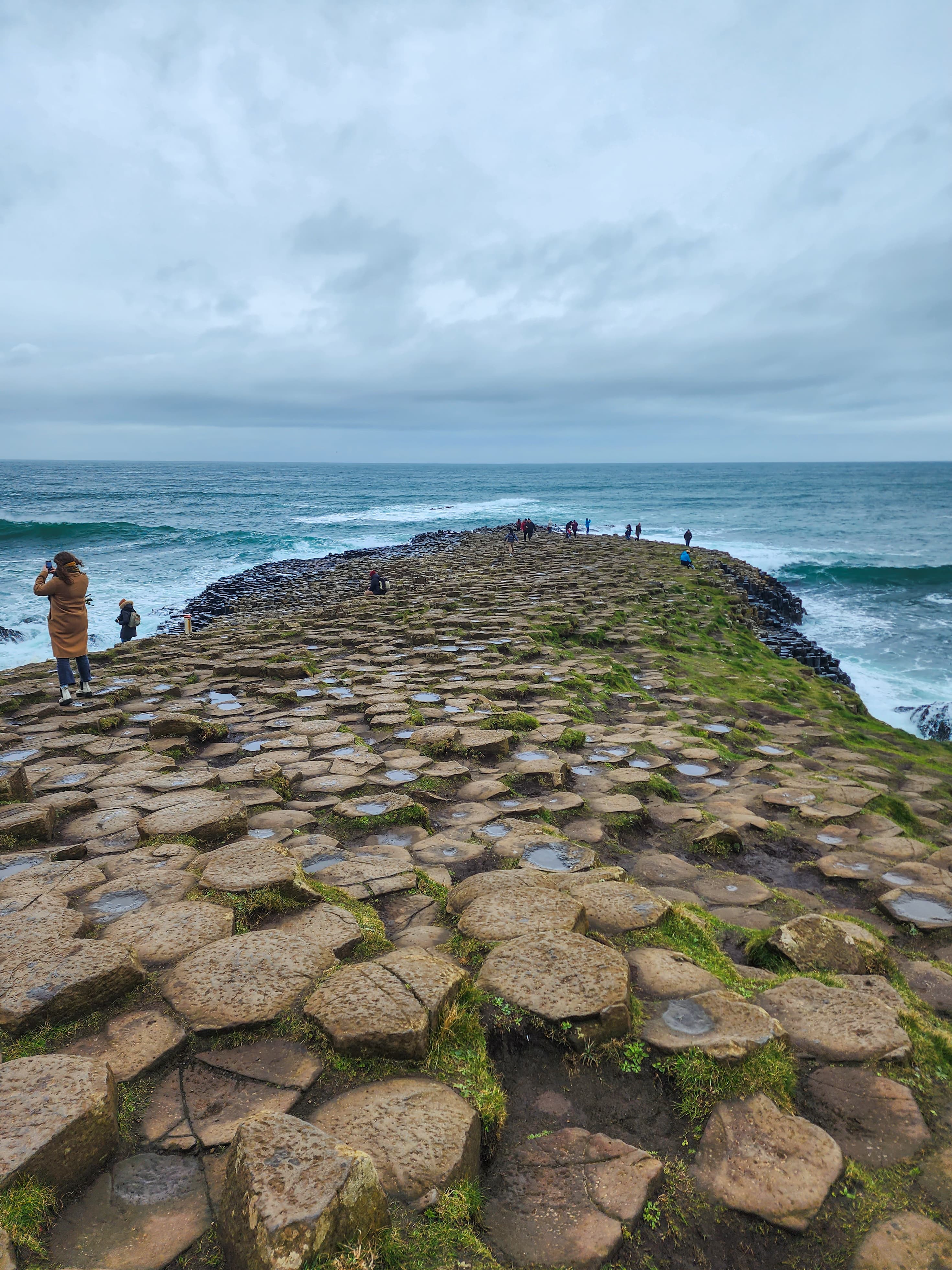 Stone pathway covered in moss leading to the ocean on a cloudy day