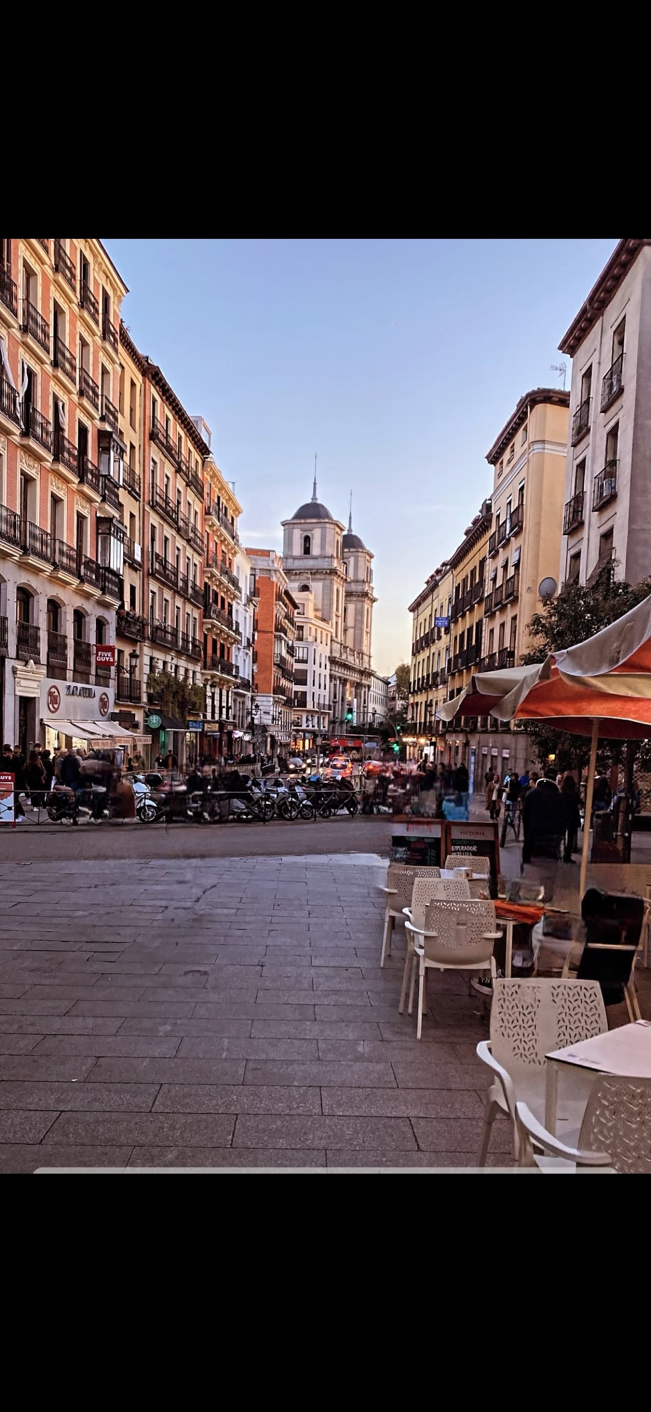 View of an empty city street lined with outdoor restaurant seating and pretty buildings