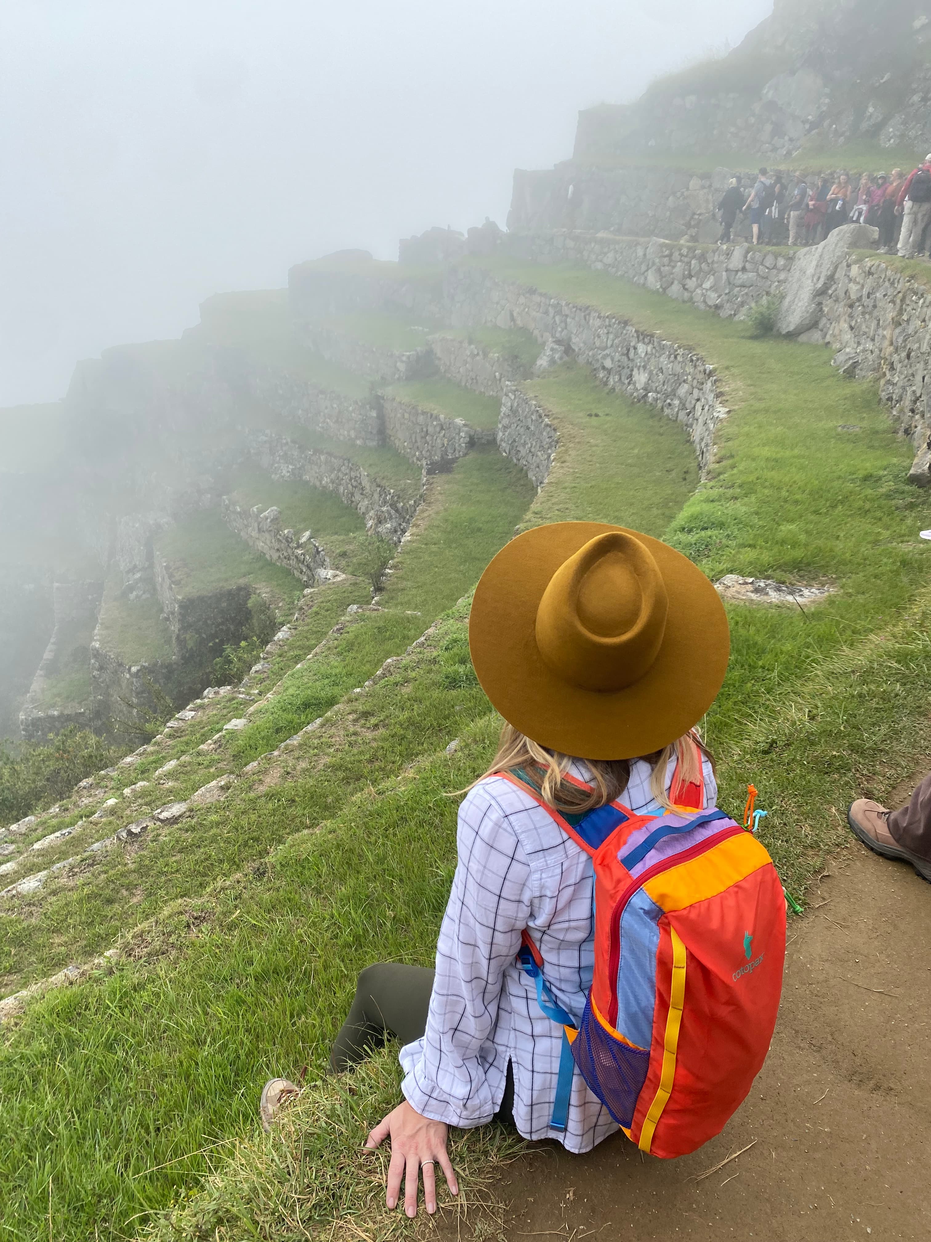 View of Angie wearing a colorful backpack on a tiered cliffside in foggy weather