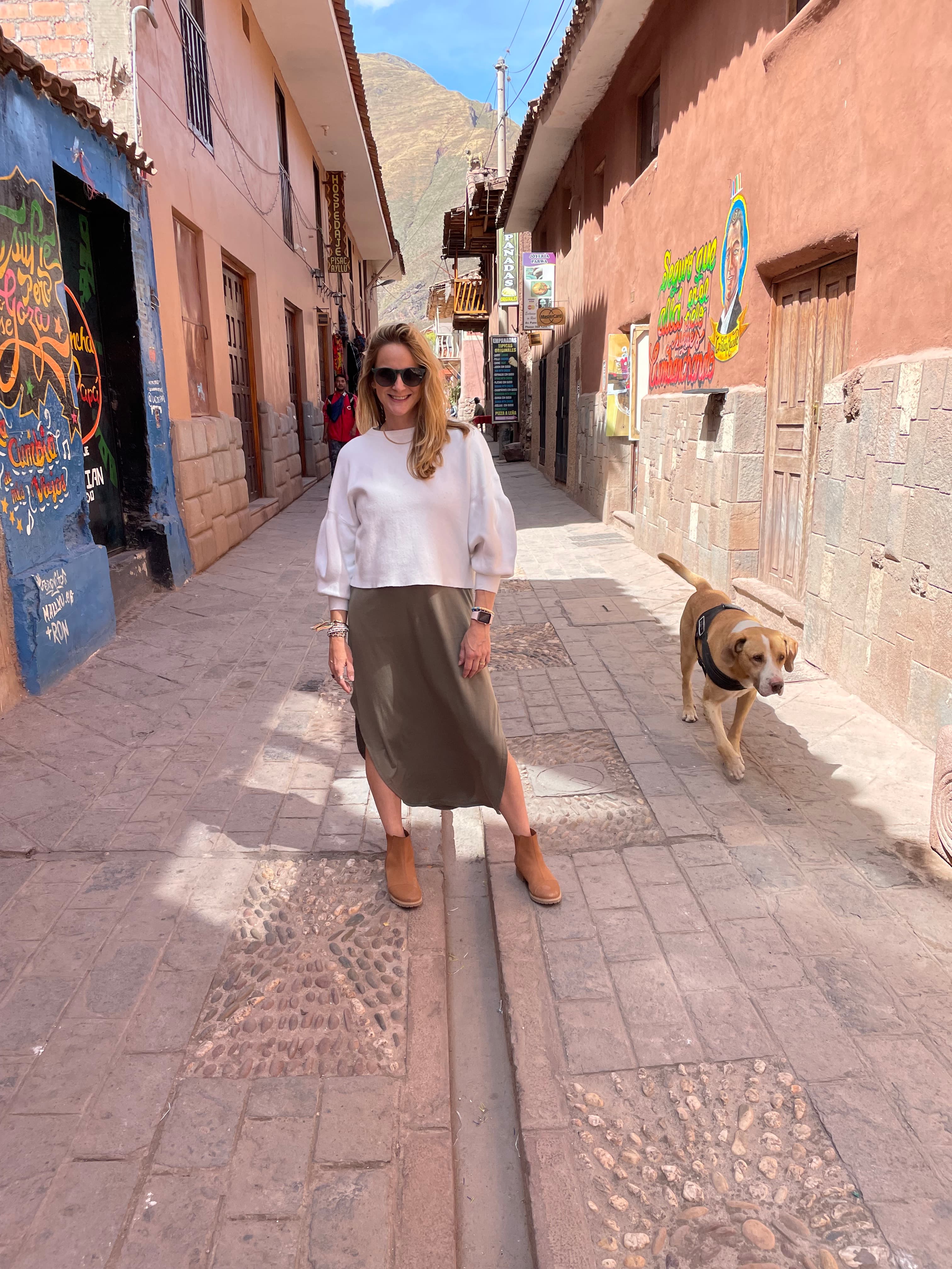 Angie posing in the middle of a narrow street with a dog next to her on a sunny day