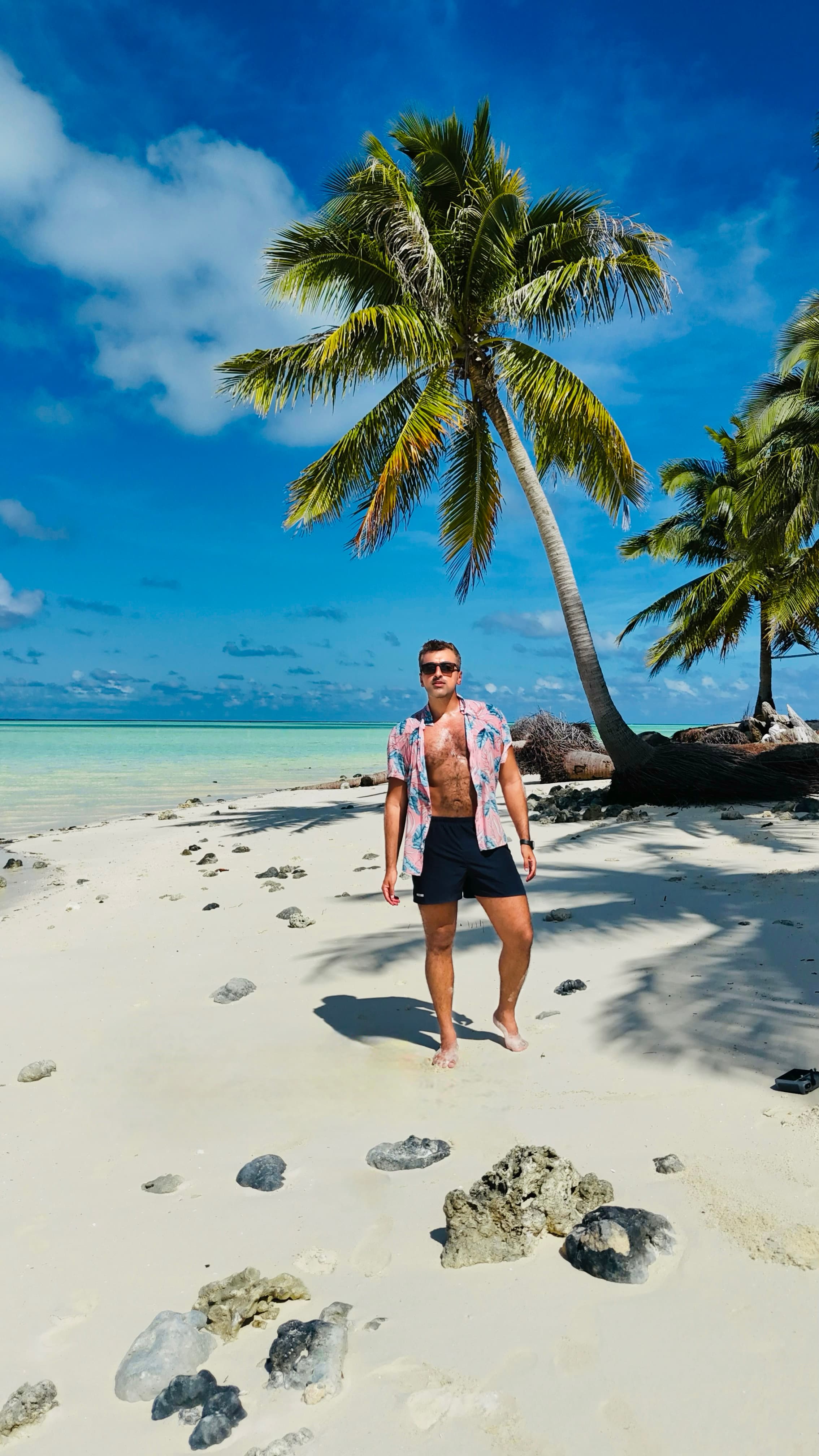 View of advisor standing on a beautiful white sandy beach with a palm tree behind him on a sunny days