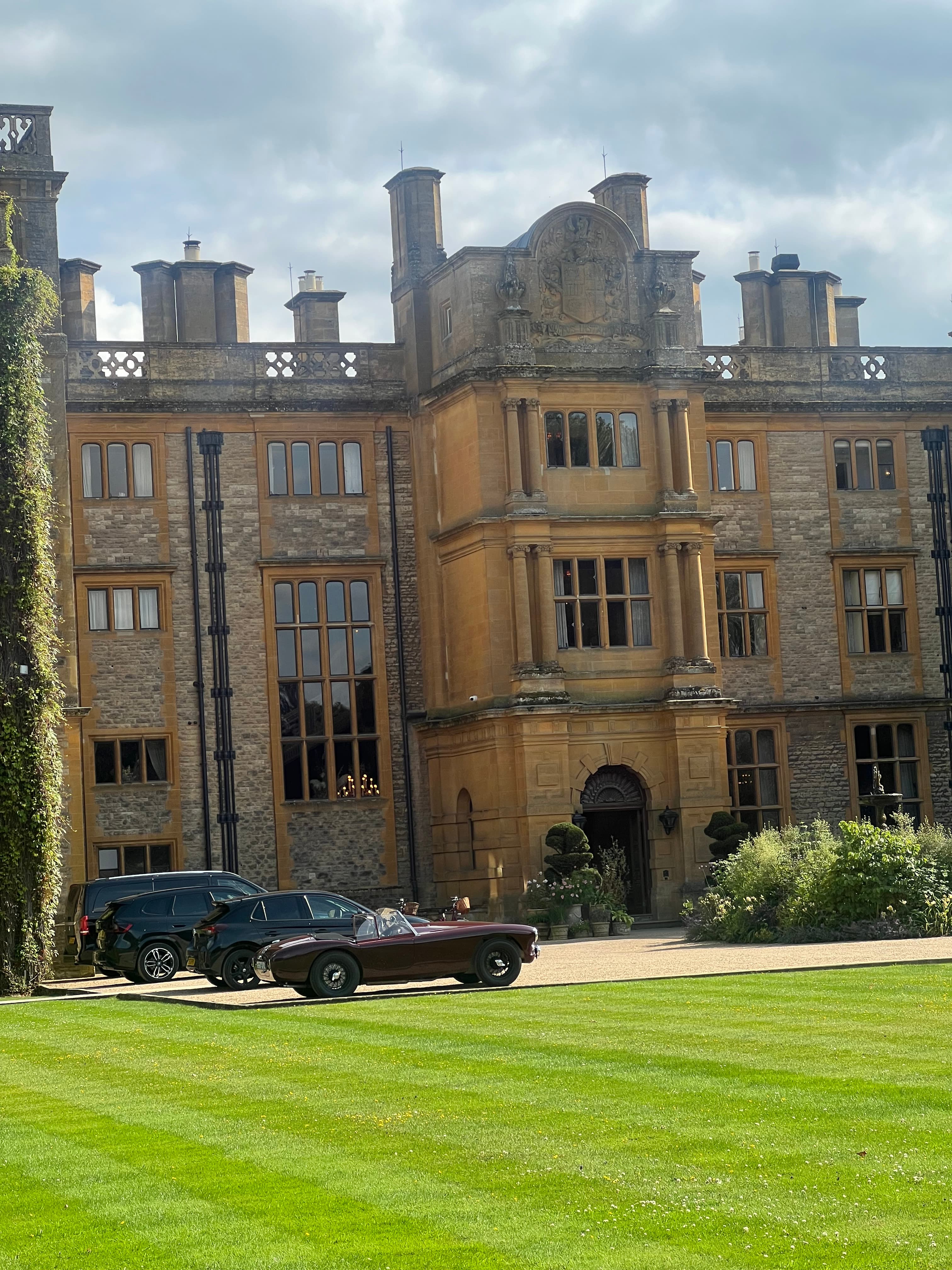 View of a beautiful estate house and green lawn with cars parked out front on a cloudy day