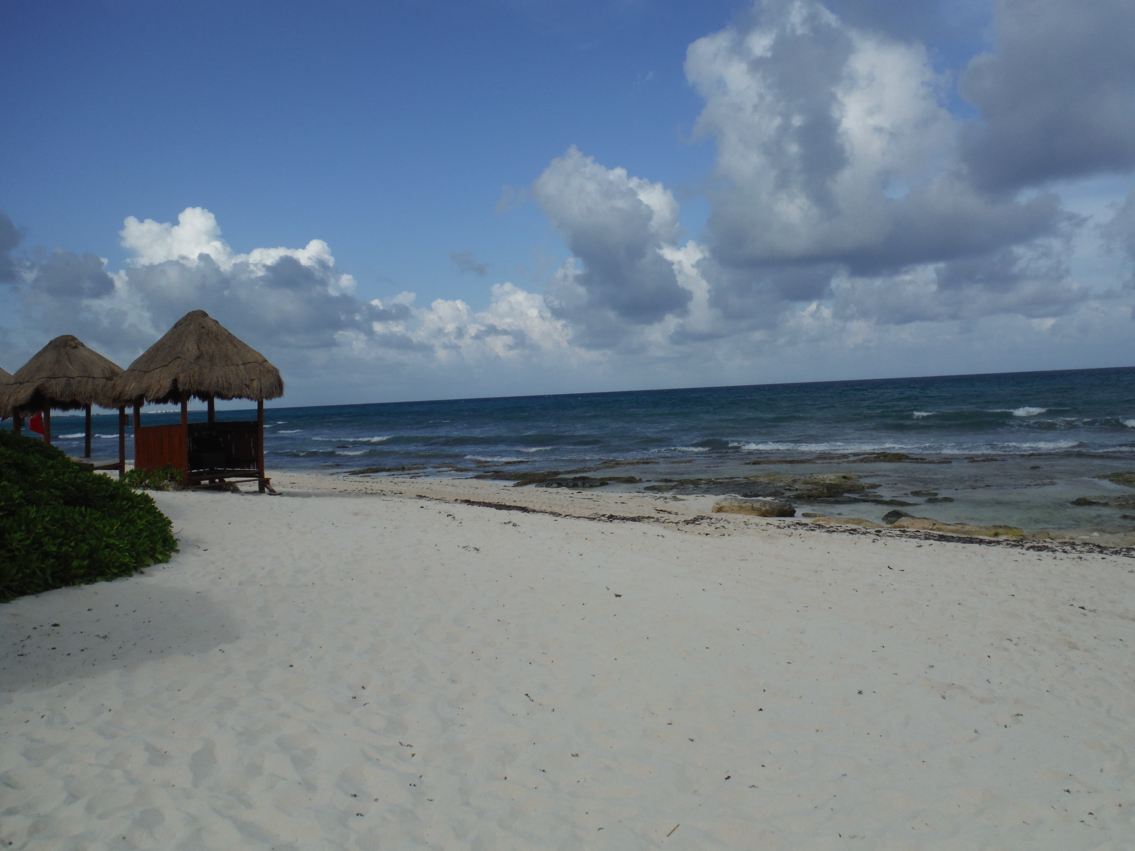 Clouds over the beach with beach huts in the distance.
