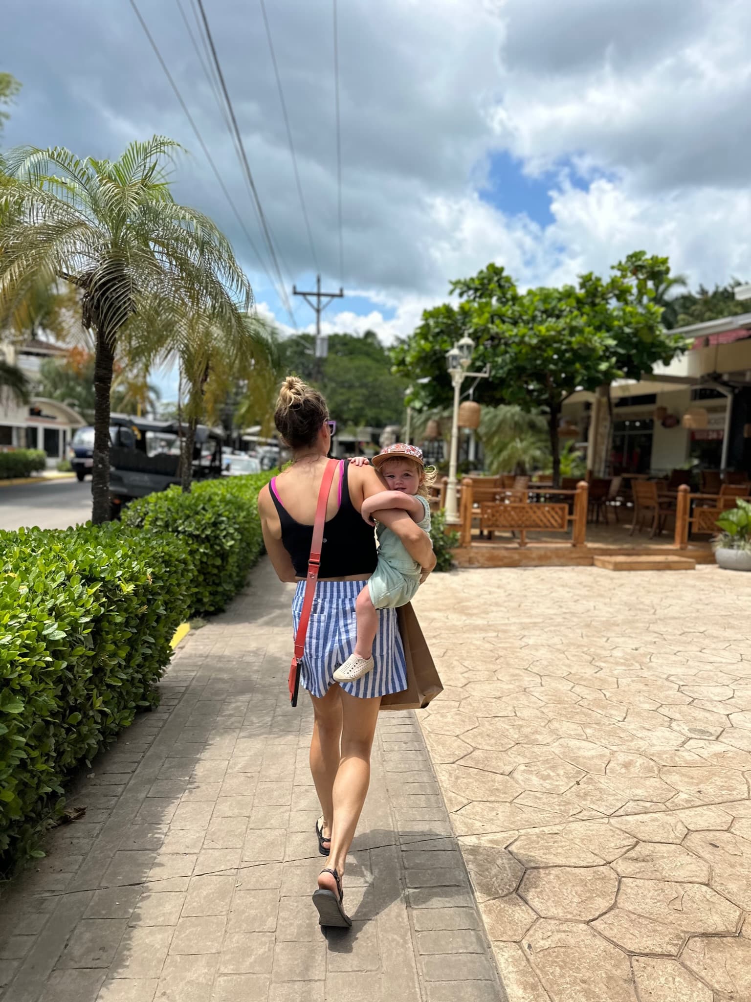 Advisor carrying a young baby on a stone path with plants alongside