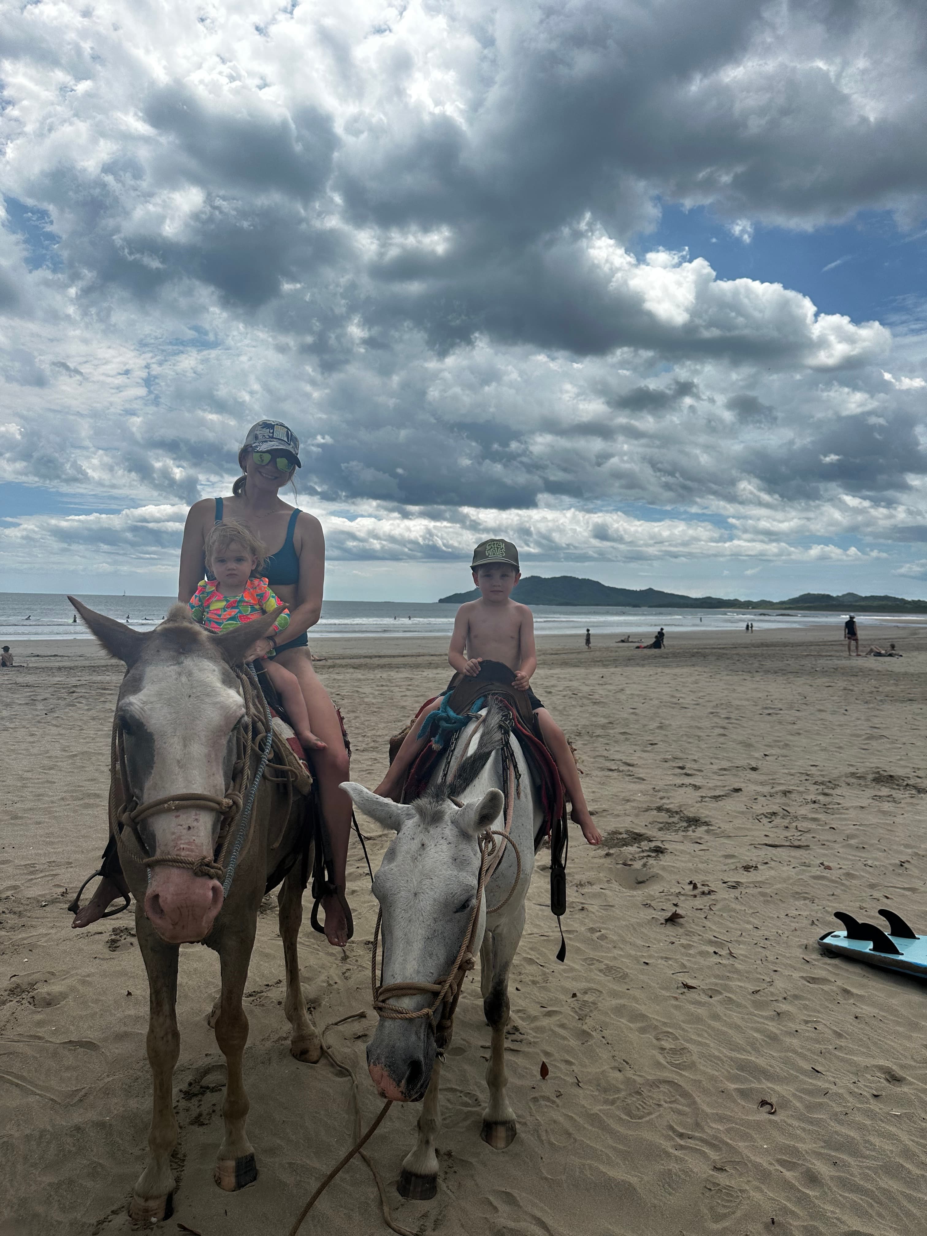 Advisor and a young child on horseback on the beach on a cloudy day