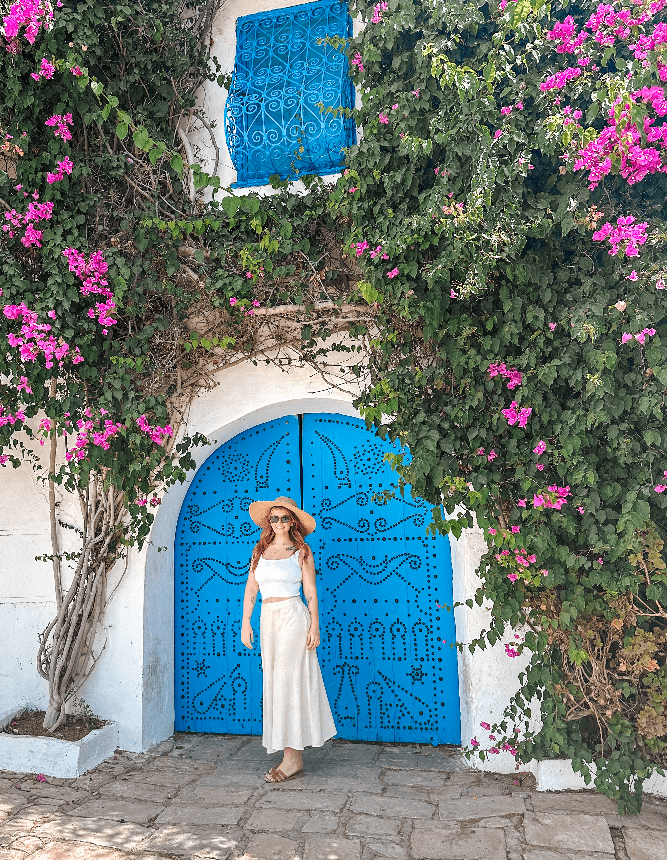 Advisor in a white dress posing in front of a blue door and a building covered in vines and purple flowers