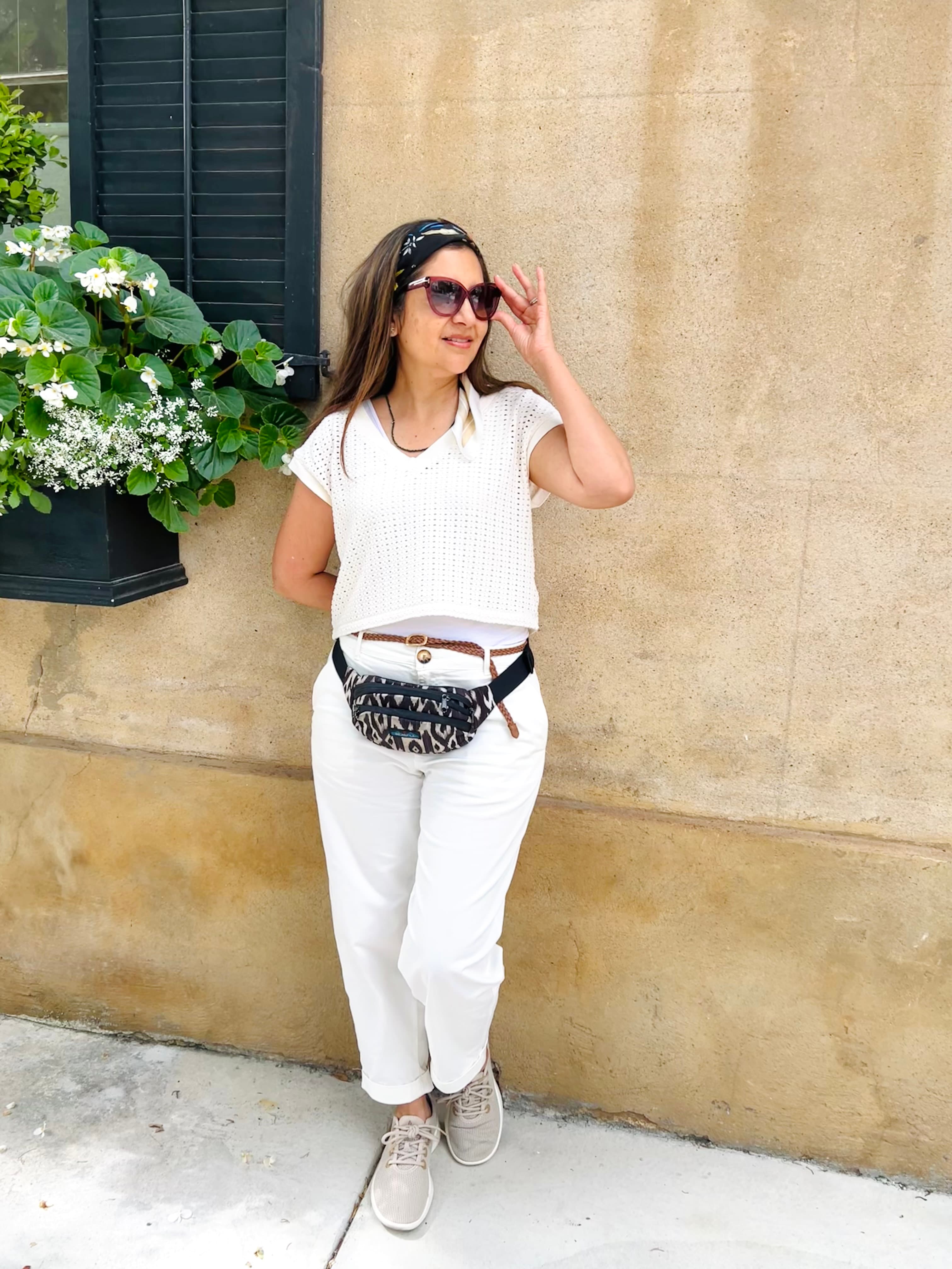 Advisor in an all-white outfit and sunglasses posing against a wall outdoors during the day