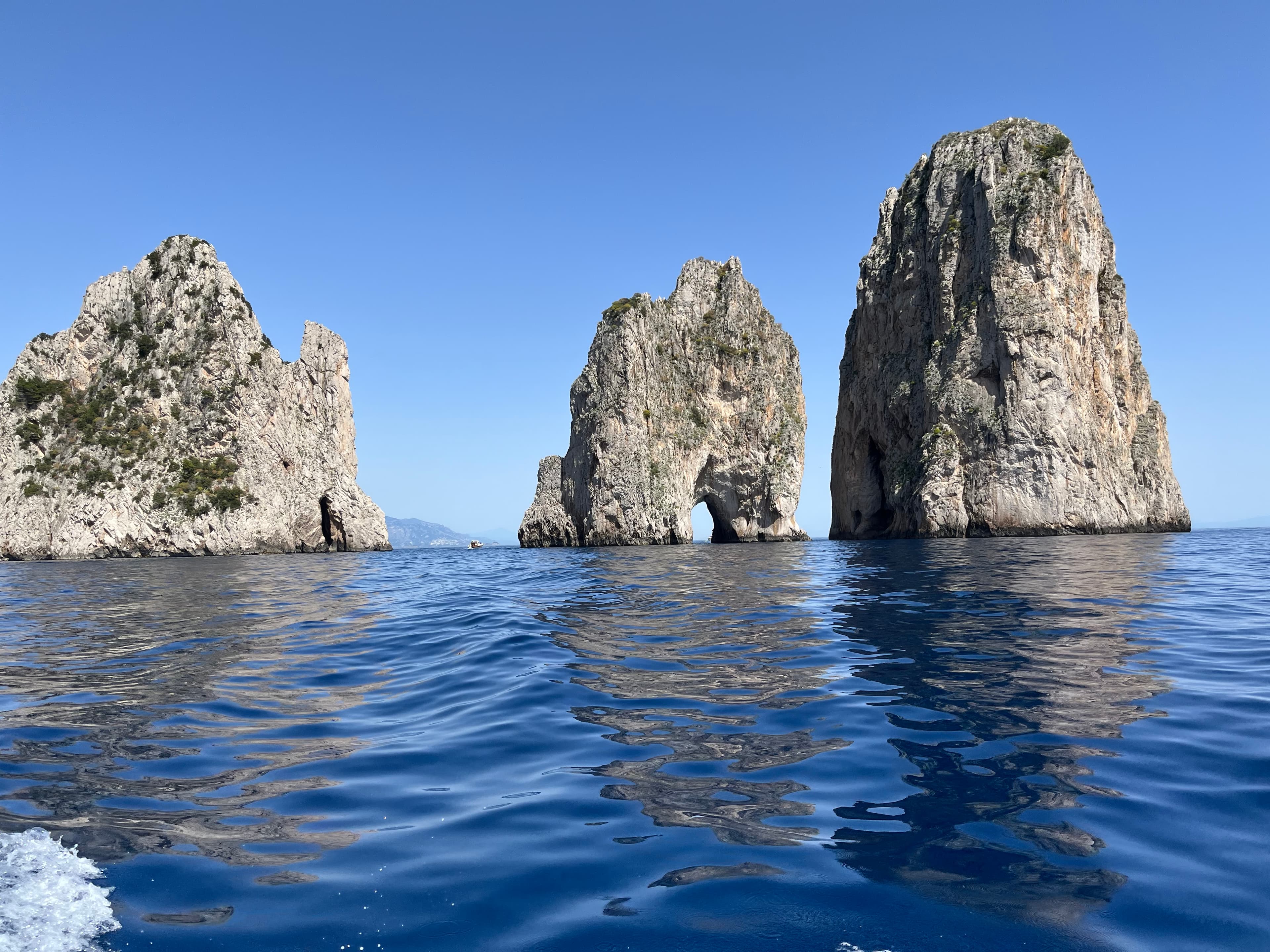 View of three large rock formations emerging out of the ocean under clear skies