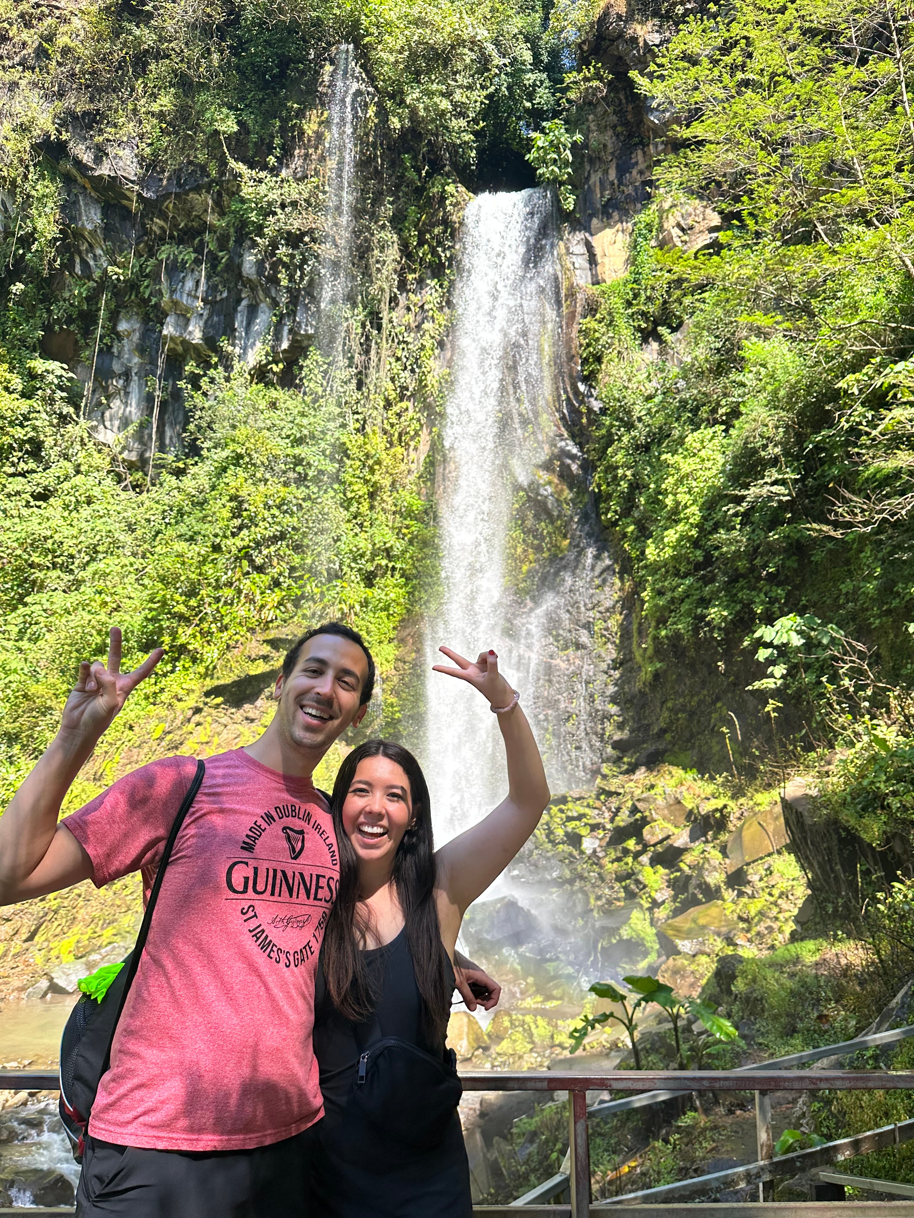 Advisor and a woman posing with peace signs by a beautiful waterfall