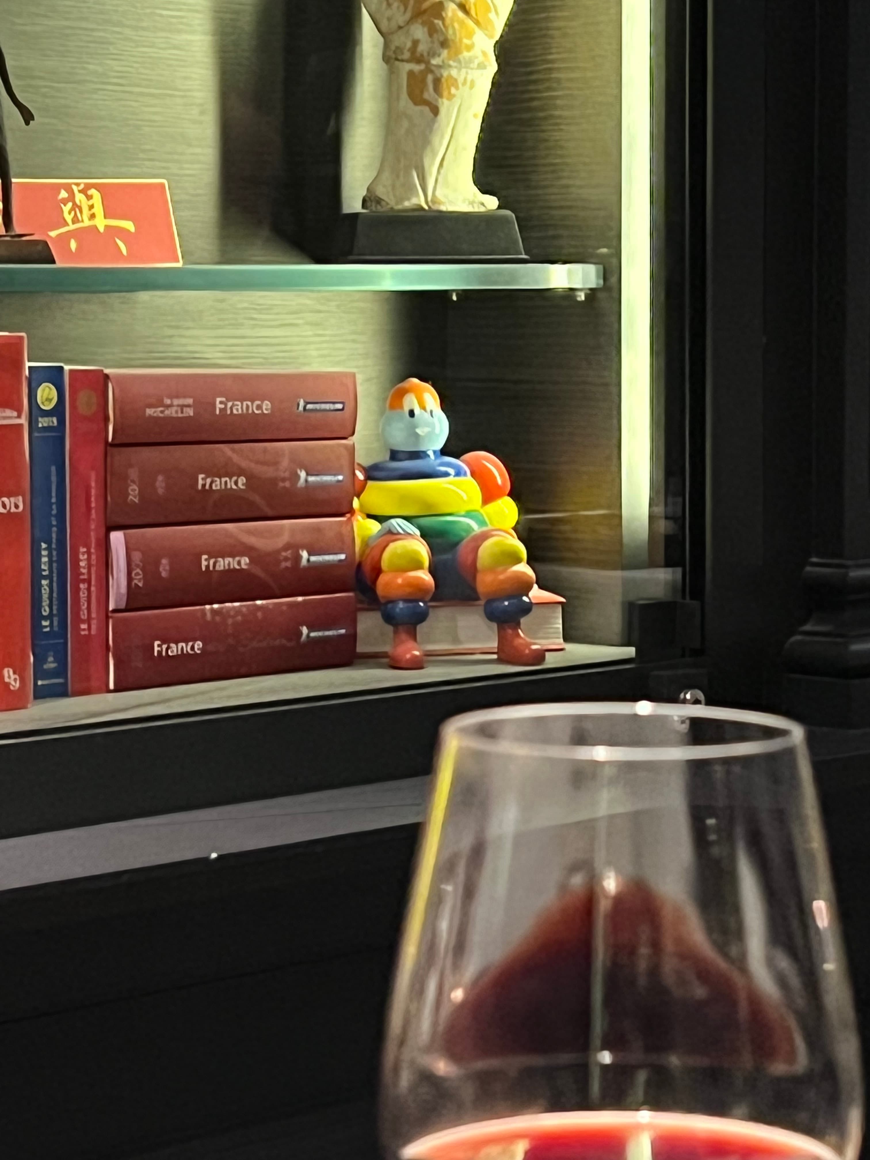 A wine glass on a table with a stack of books on a shelf in the background.