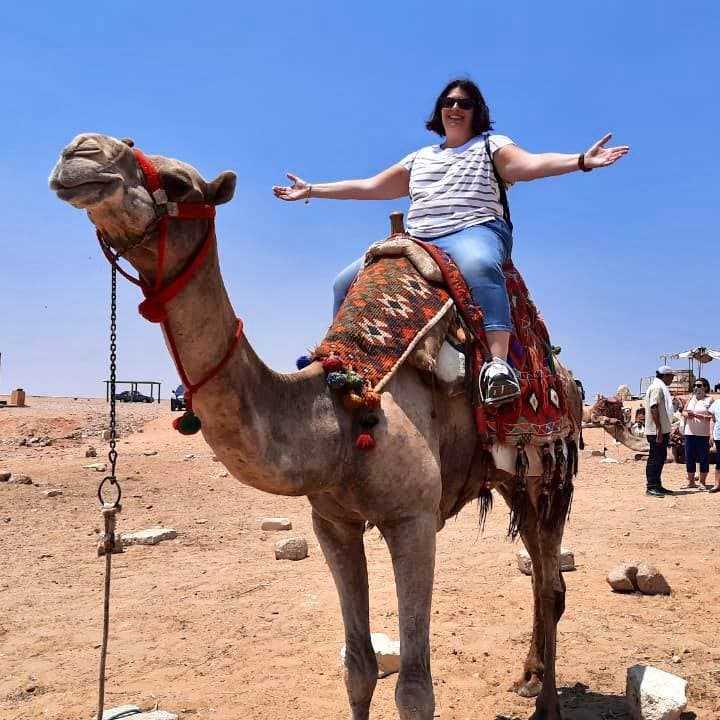 Advisor sitting on a camel’s back with arms outstretched on a sunny day