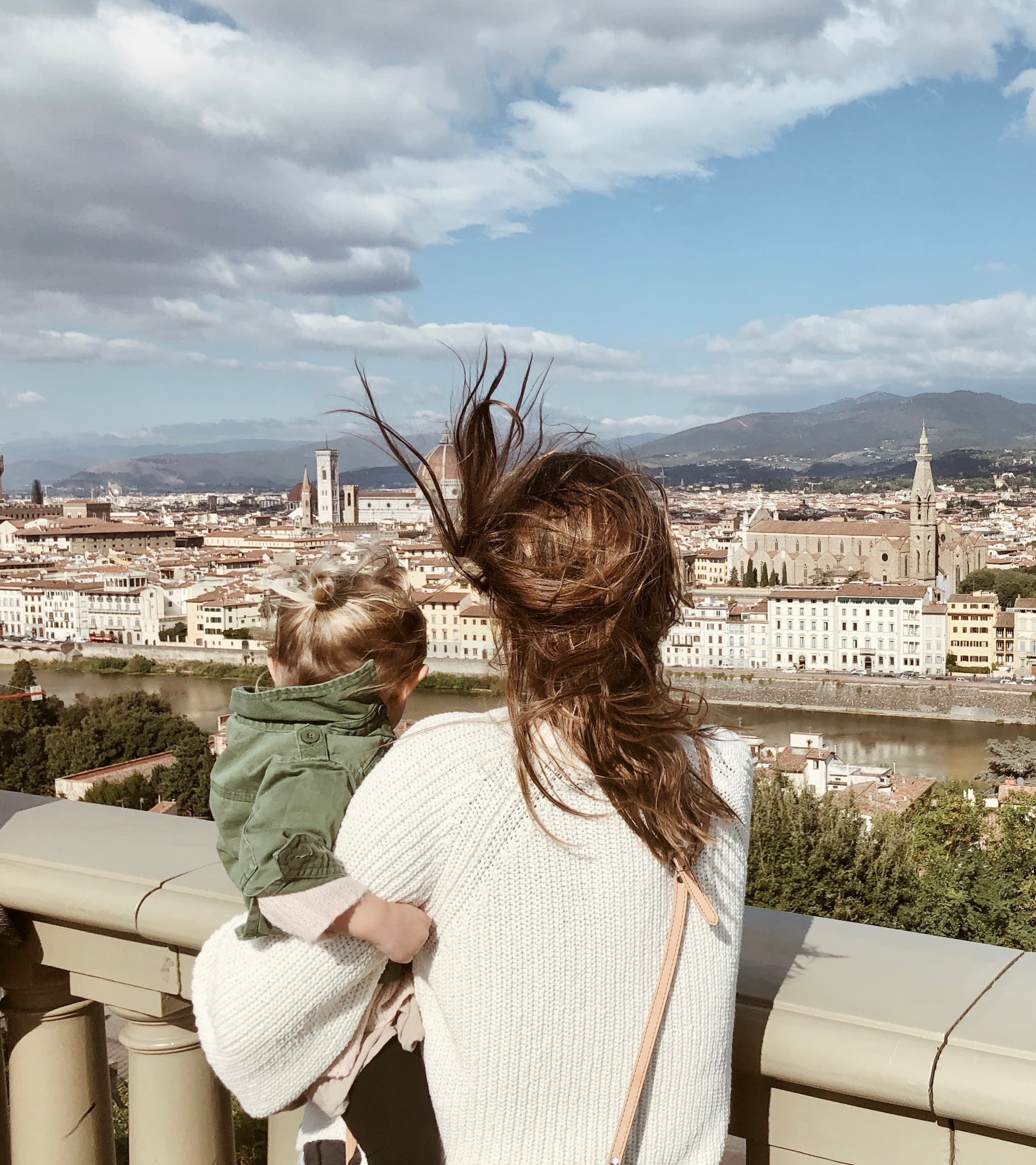 Advisor with windblown hair holds a toddler and looks out over a city skyline.