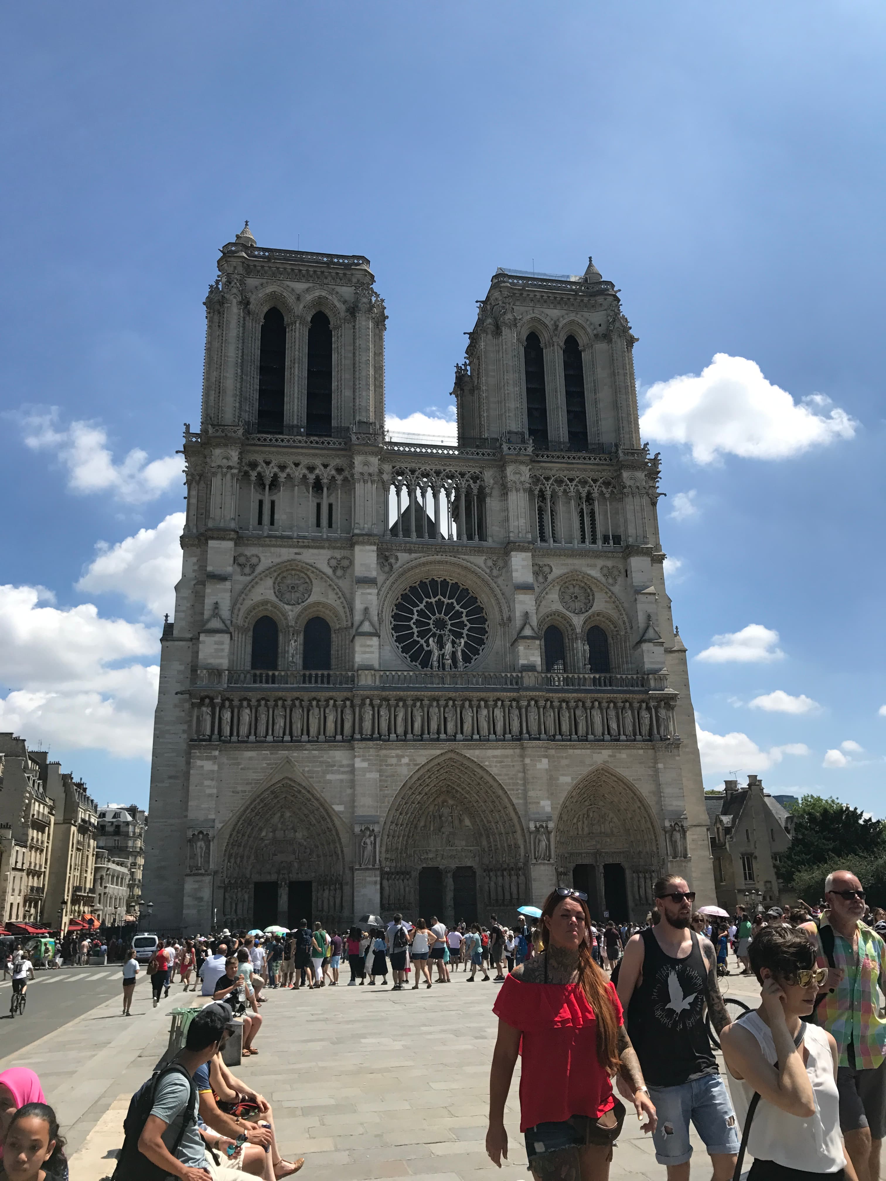 A view of the Notre Dame cathedral with tourists walking around in front of it. 