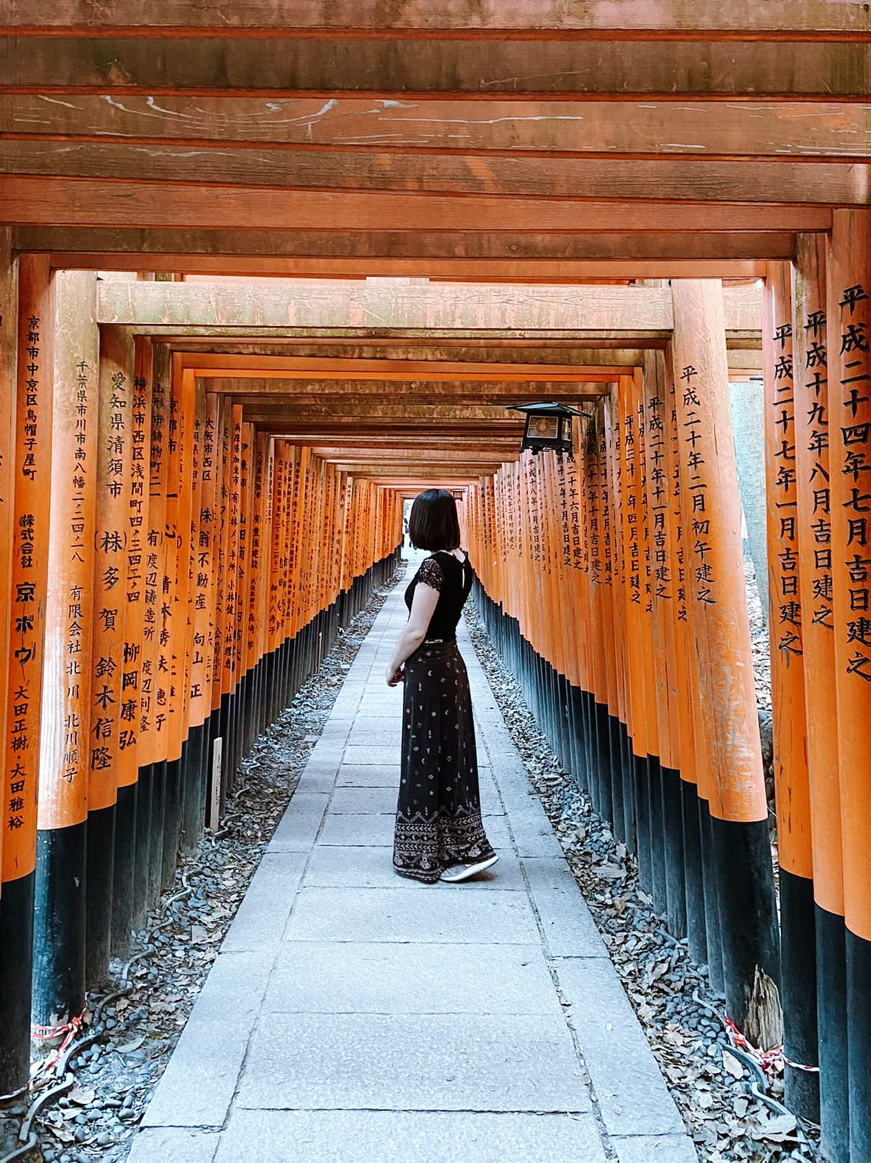 A woman posing outside in Japan beneath a red archway. 
