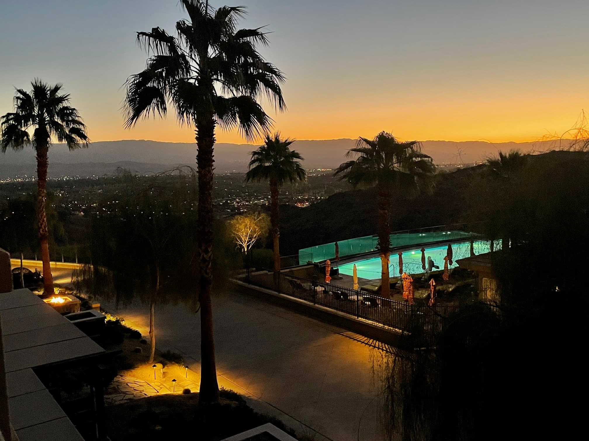 View of palm trees and an illuminated resort pool at sunset