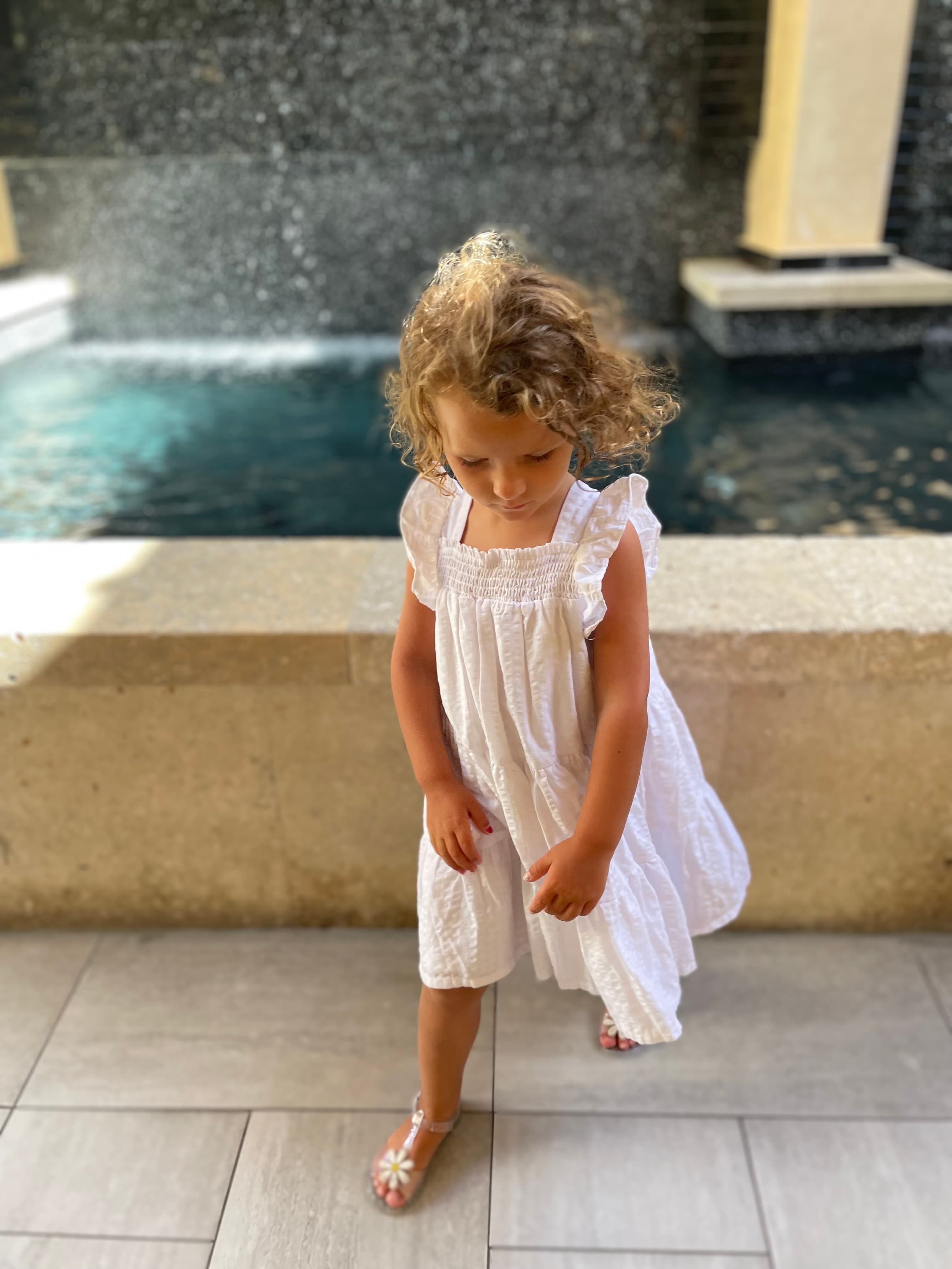 Young girl in a white dress walking in front of a fountain