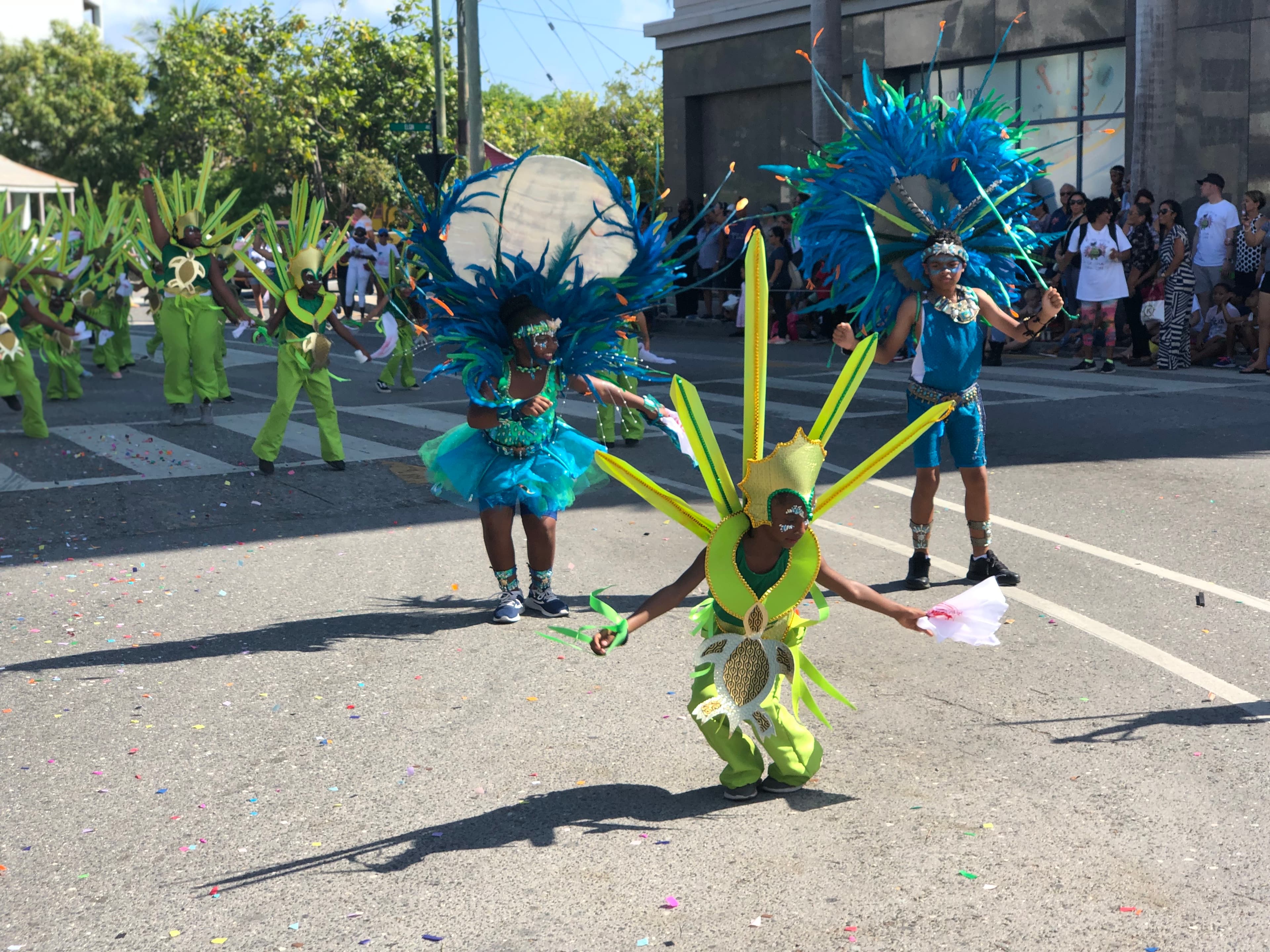 A parade of participants in brightly colored costumes dancing in the street on a sunny day.